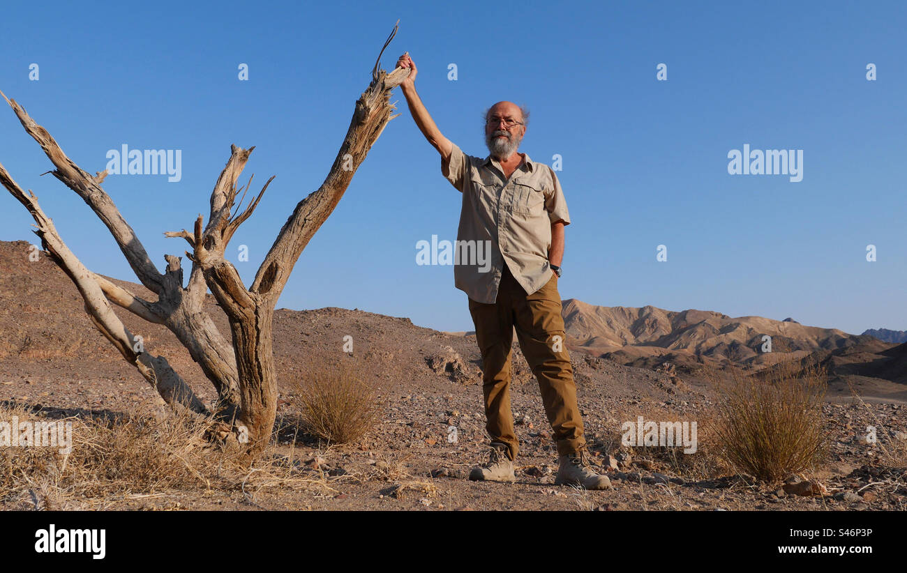 Älterer Mann, der in der Wüste in der Nähe eines Baumes steht Stockfoto