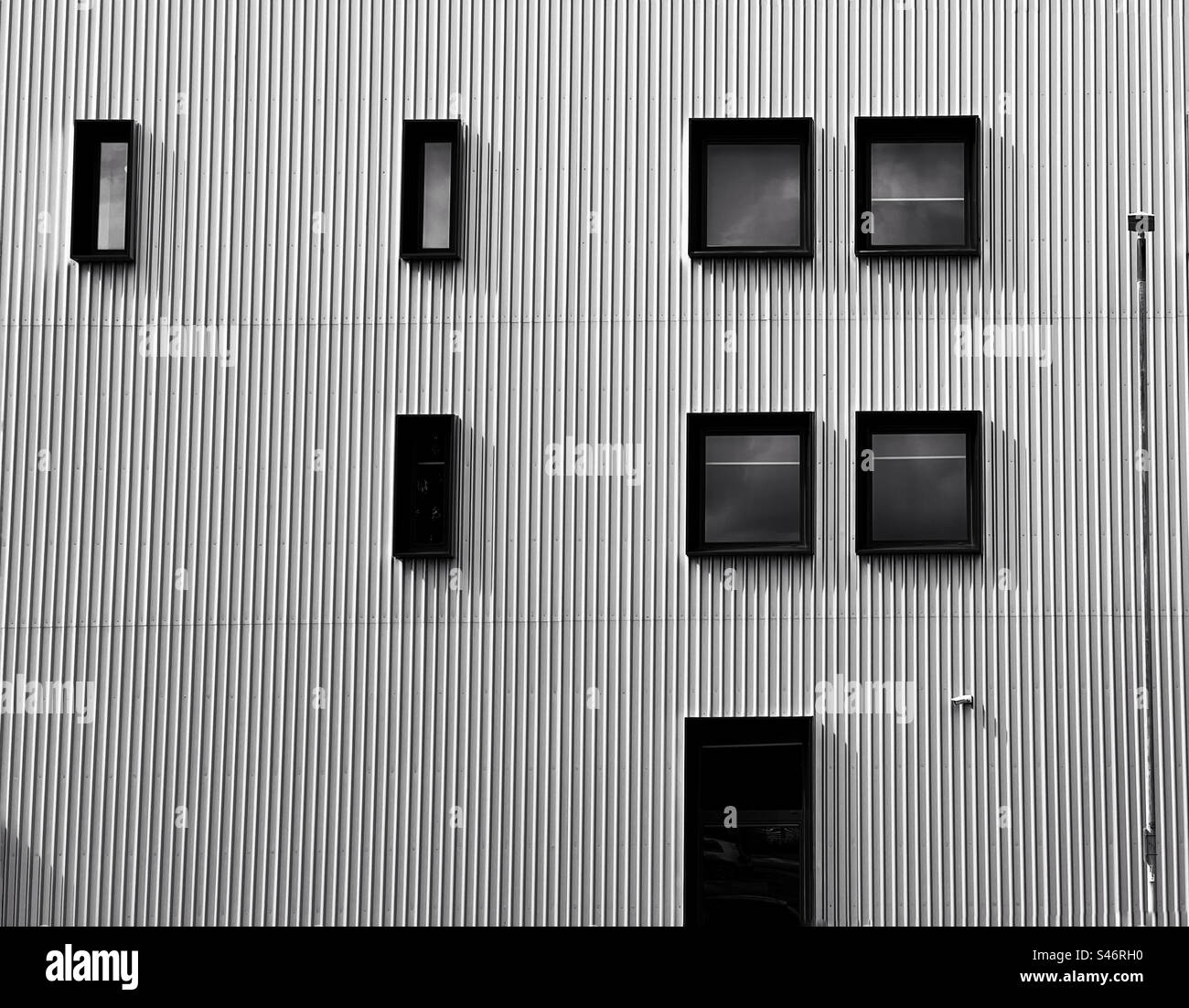 Abstrakte, wenn schwarz gerahmte rechteckige Fenster in gewellter Metallwand in einem modernen Gebäude in Bolton Stockfoto
