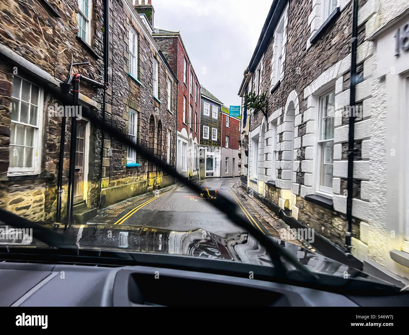 Wir fahren mit dem Auto durch eine sehr enge Straße auf der Church Street in Mevagissey in Cornwall, Großbritannien Stockfoto