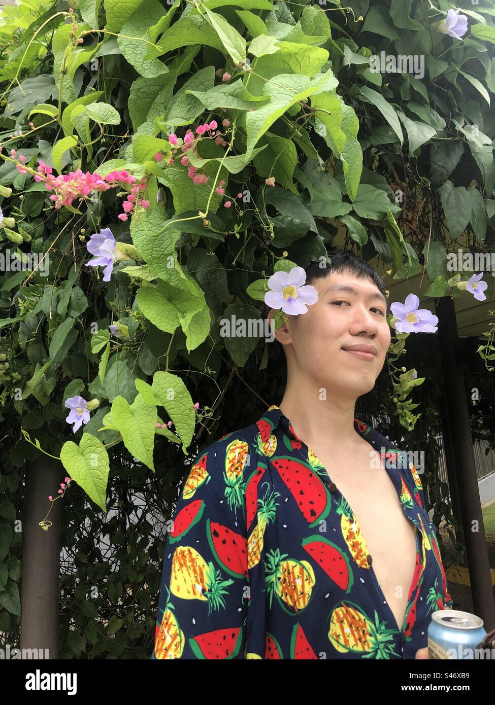 Gutaussehender schwuler Kerl, der tropische Früchte vor einem Blumenbaum trägt Stockfoto