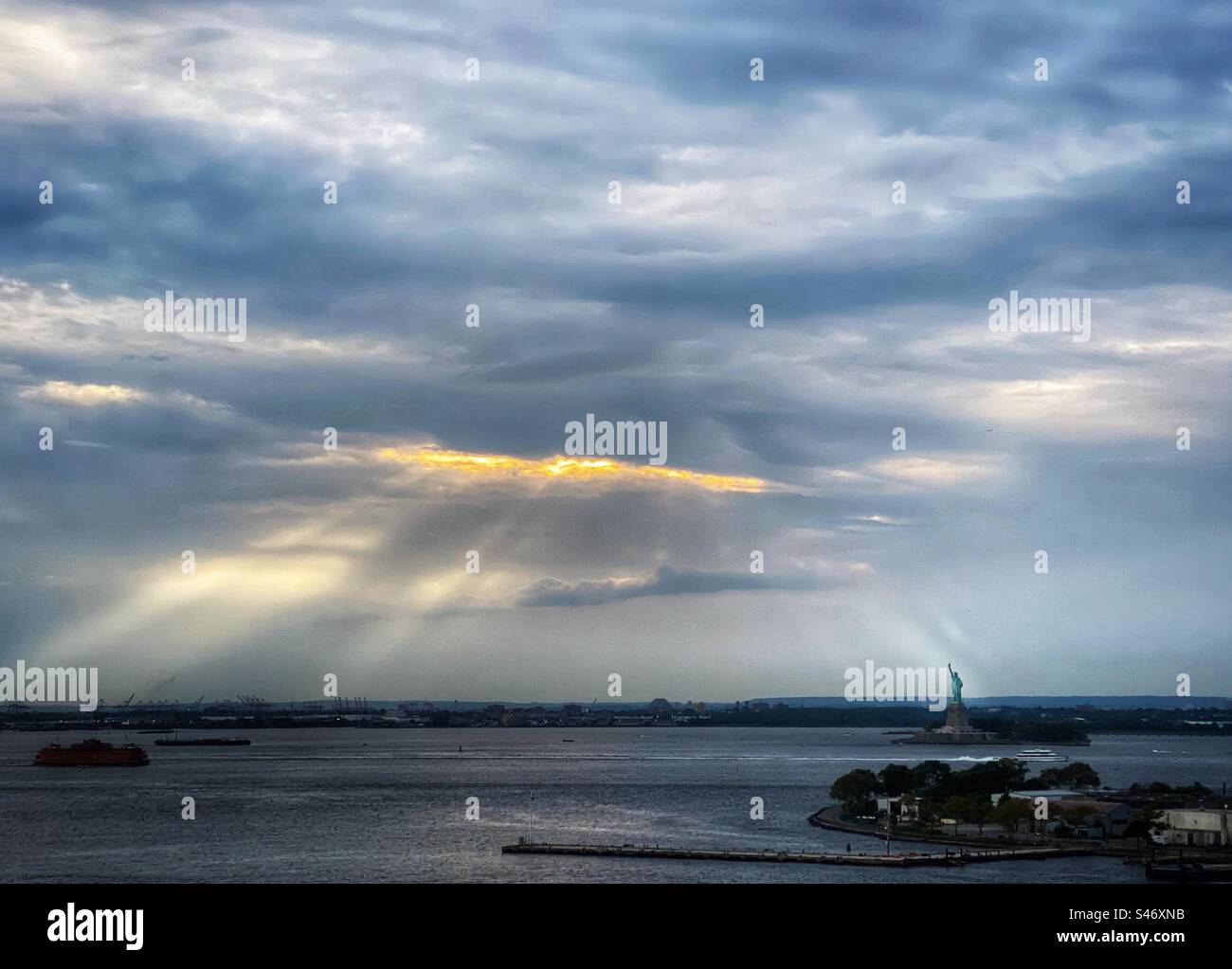 Sonnenlicht bricht durch Wolken und scheint auf der Freiheitsstatue im Hafen von New York - Smartphone-aufgenommenes Stockfoto