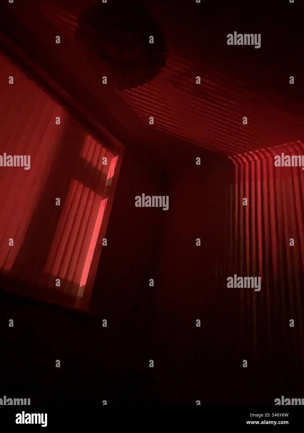Ein leeres Zimmer und ein nachts beleuchtetes Fenster mit tiefrotem Licht - Schatten Innenraum Hintergrund Kopierraum dunkel - Smartphone-aufgenommenes Stockfoto
