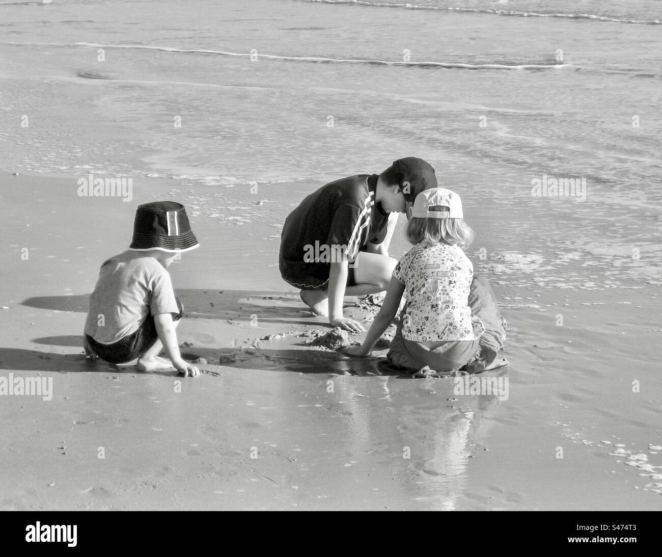 Drei Kinder spielen an einem Strand in schwarz-weiß. - Smartphone-aufgenommenes Stockfoto