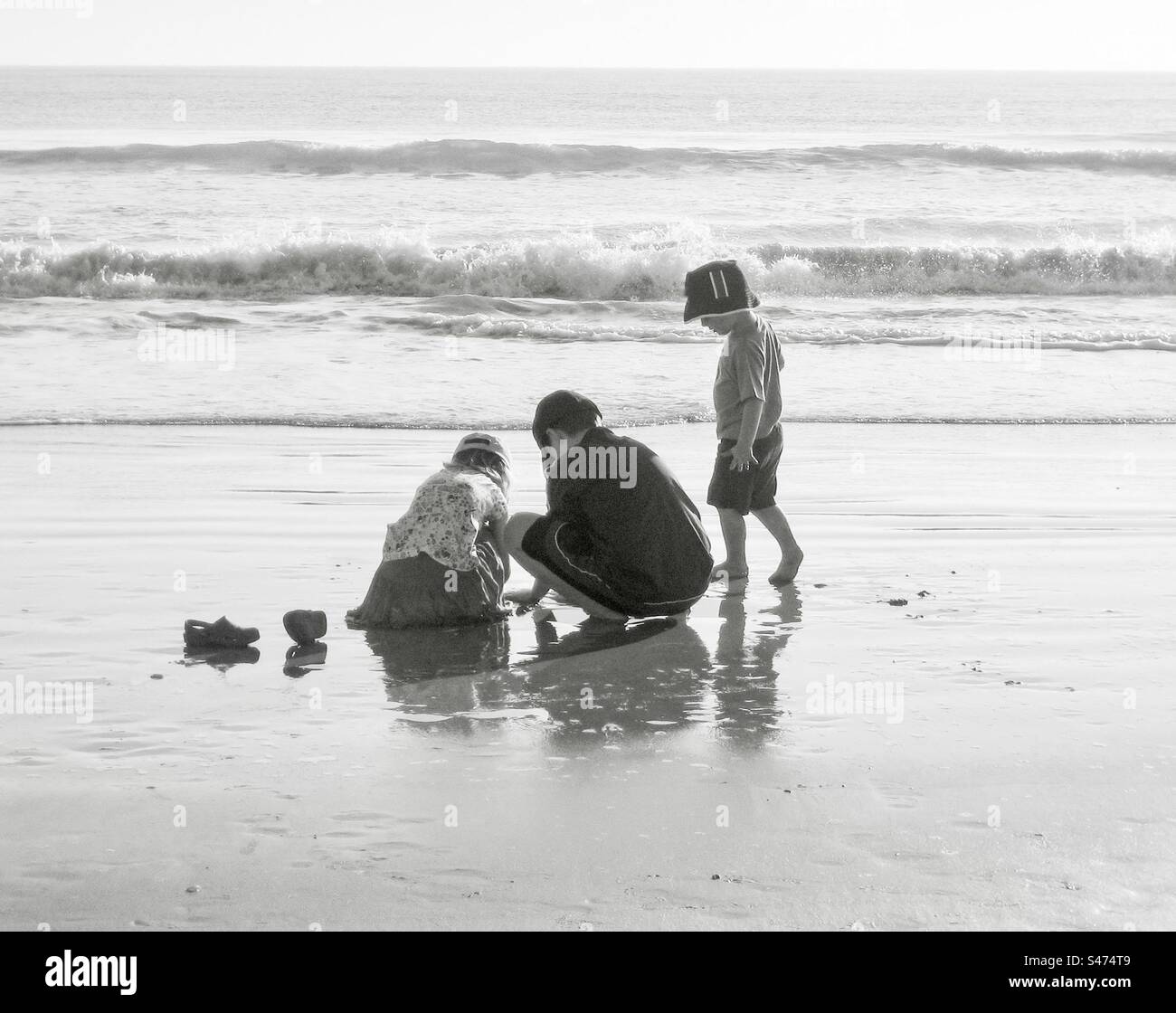 Drei Kinder spielen an einem Strand in schwarz-weiß. - Smartphone-aufgenommenes Stockfoto