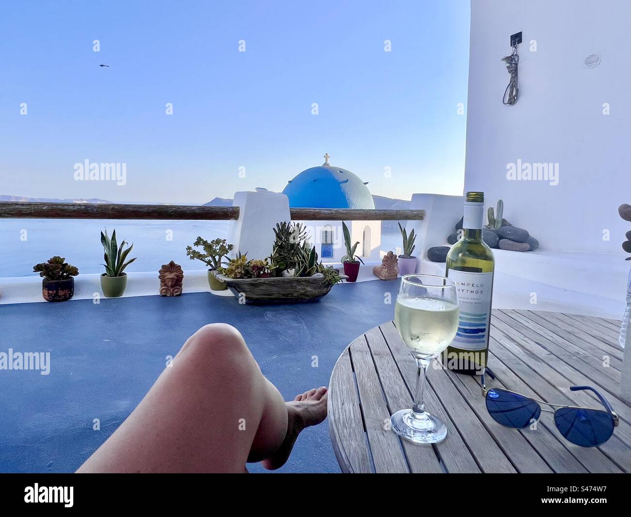 Am frühen Abend entspannen Sie bei einem Glas Wein mit Blick auf die Anastasi-Kirche mit ihrer blauen Kuppel in Oia, Santorin. Stockfoto