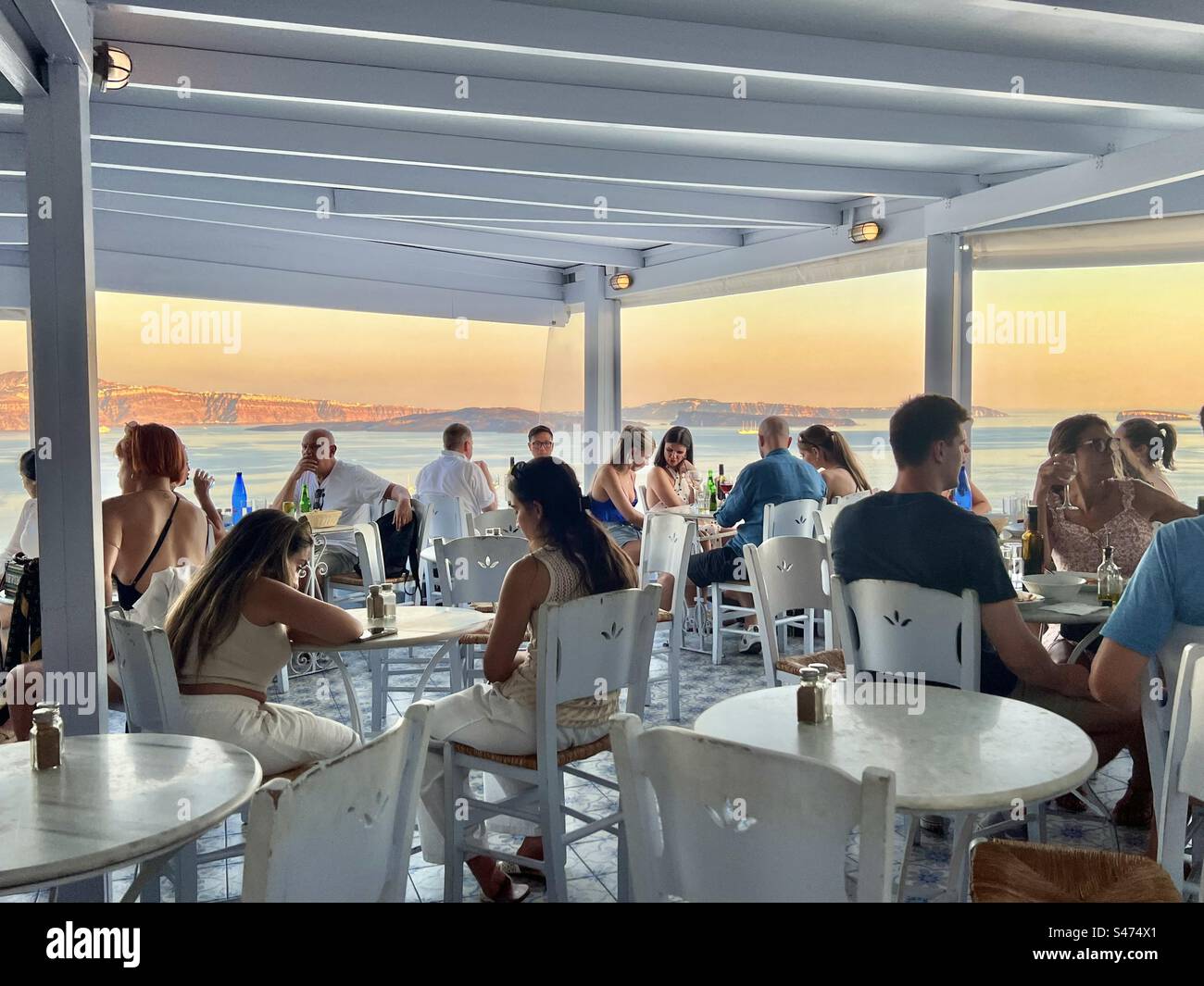 Gäste des Restaurants können von Oia, Santorin, aus das Licht der untergehenden Sonne über der Ägäis genießen. - Smartphone-aufgenommenes Stockfoto