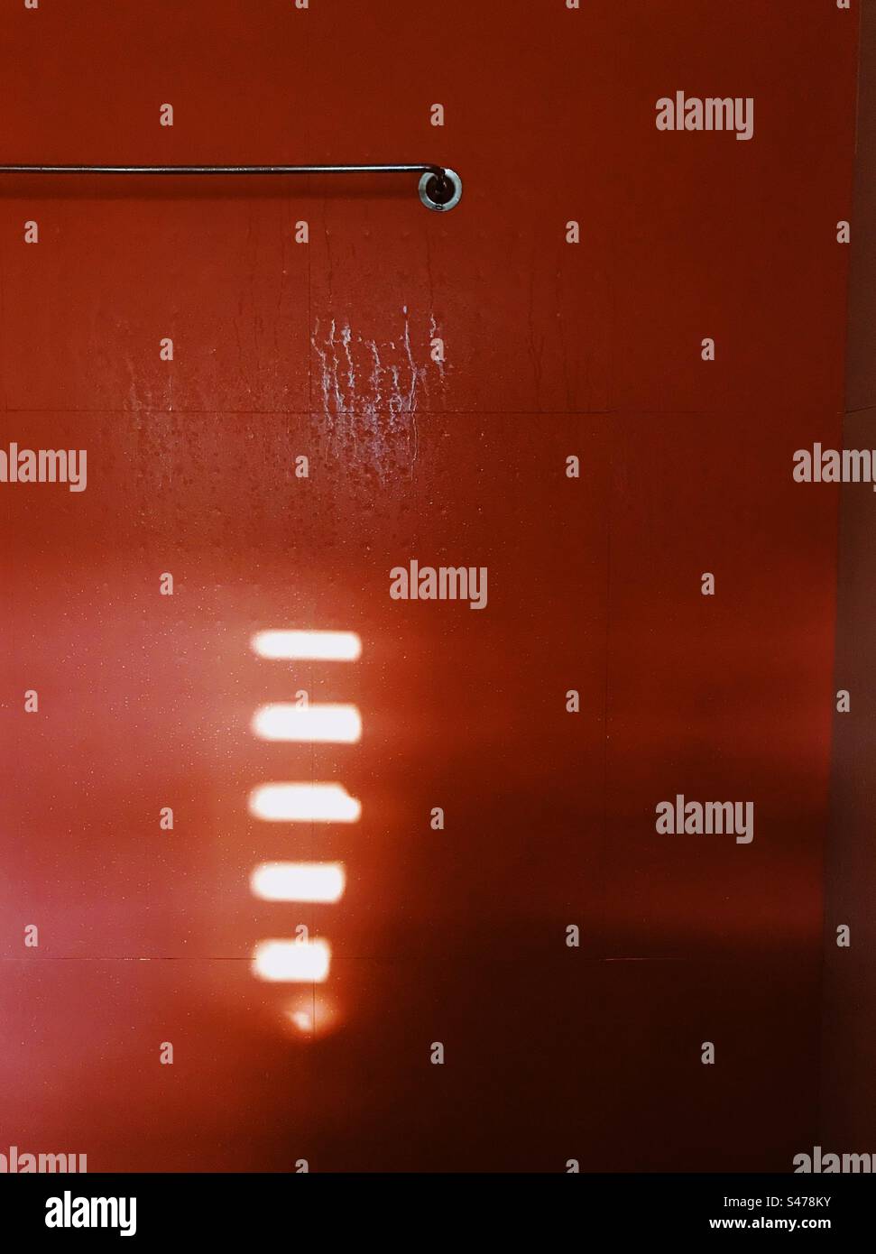 Rote Fliesen an einer Badezimmerwand mit Wassertropfen und Licht, das durch ein Fenster kommt - Smartphone-aufgenommenes Stockfoto