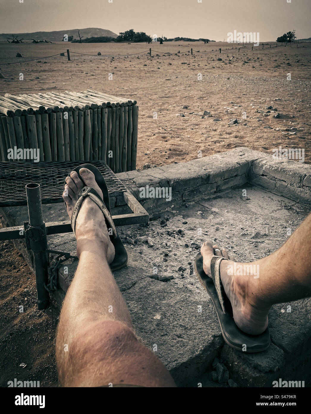 Ein Mann in Sandalen legt seine Beine auf einem grill, während er sich entspannt, während die Sonne in Namibia untergeht Stockfoto