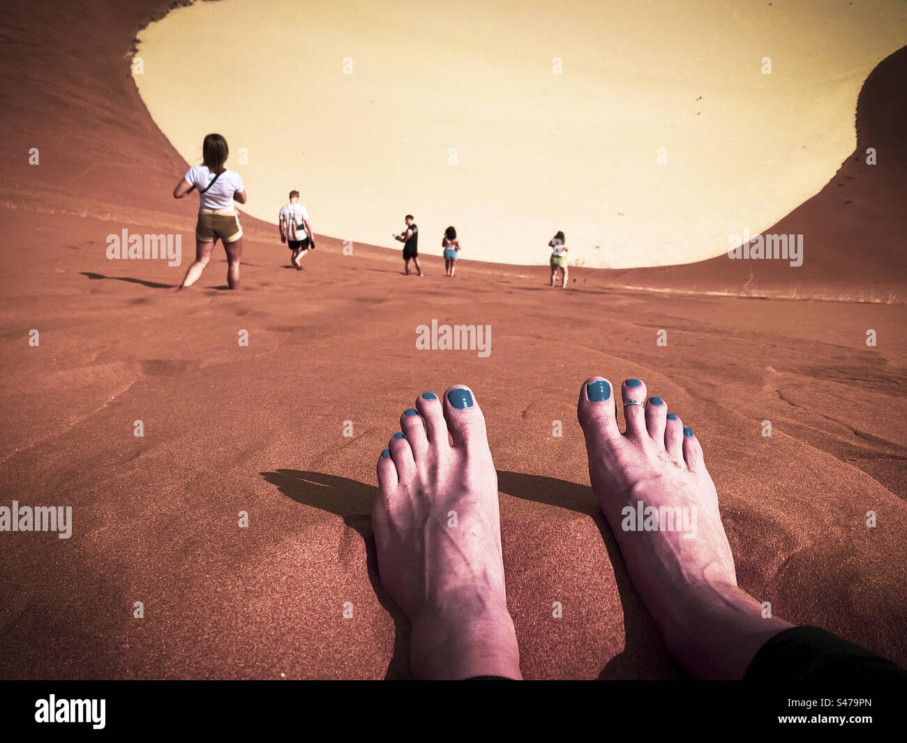 Zwei Fuß auf der Spitze einer Sanddüne, während die Leute Spaß haben, den Sand in Sossusvlei in Namibia hinunter zu laufen - Smartphone-aufgenommenes Stockfoto