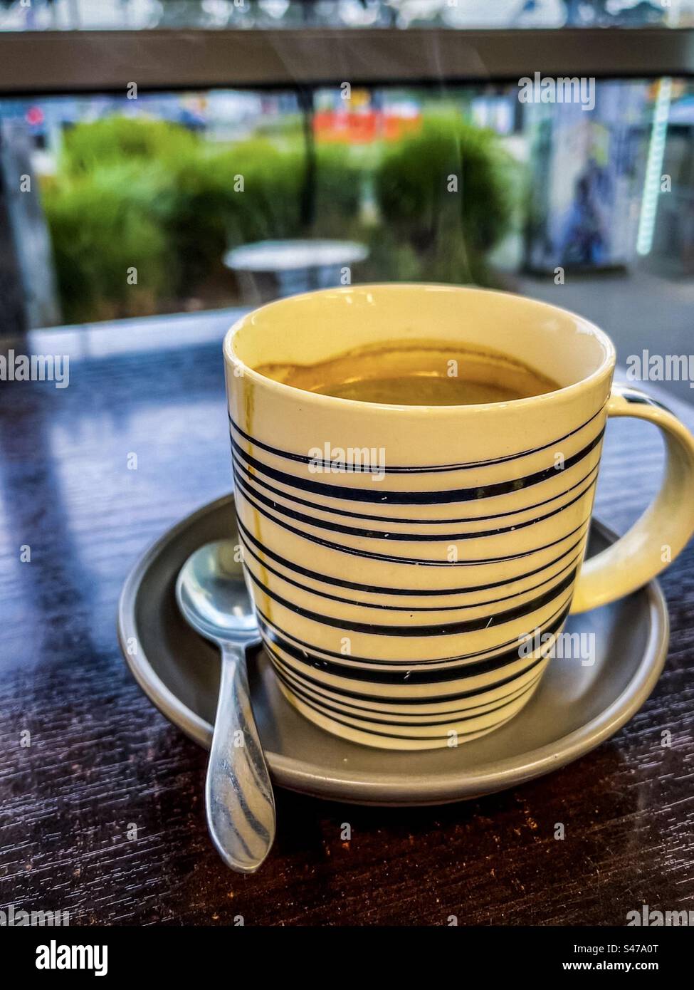Nahaufnahme des dampfenden heißen Kaffees in einer Tasse und Untertasse auf dem Tisch vor einem Fenster im Café. Erfrischung. Heißgetränk. Stockfoto
