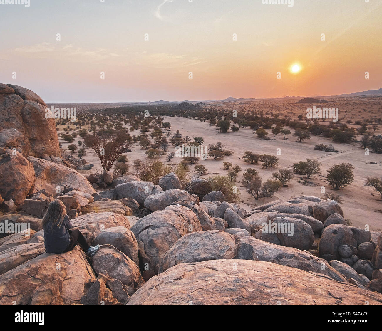 Eine Frau sitzt auf einigen großen Felsen, um einen perfekten Sonnenuntergang in Erongo Namibia zu genießen Stockfoto