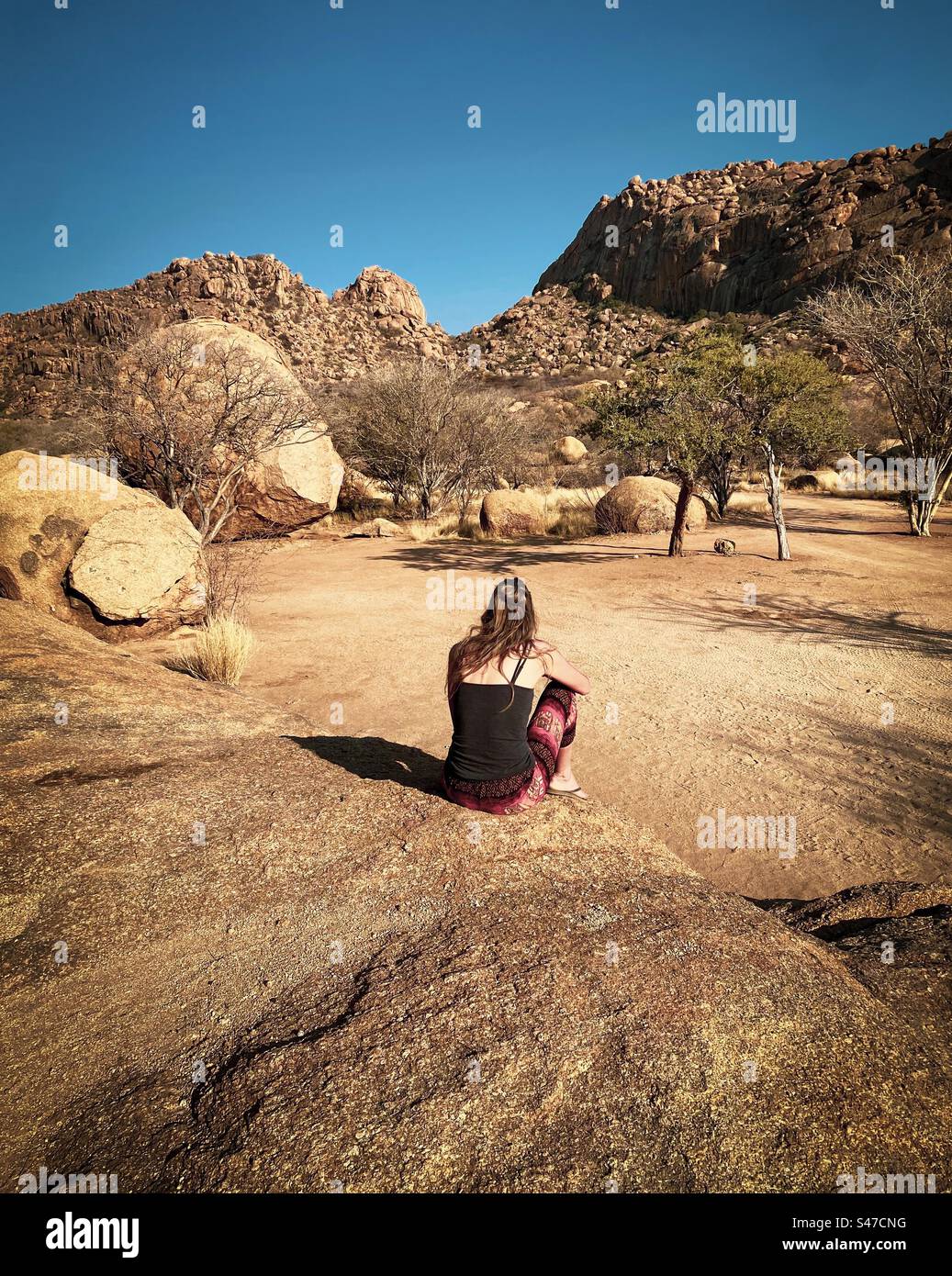 Eine Frau frühstückt, während sie auf einem großen Felsen auf einem Campingplatz in Erongo Namibia sitzt Stockfoto