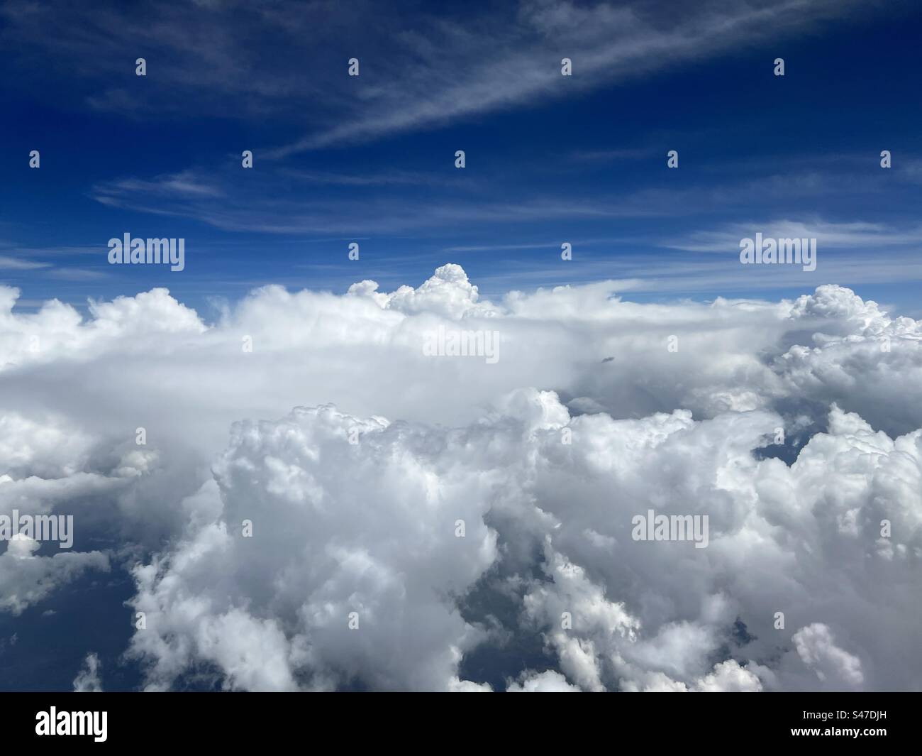 Weite Luft, Cumulus-Wolken unten, Zirruswolken mit tiefem blauen Himmel oben, durch Flugzeugfenster gesehen - Smartphone-aufgenommenes Stockfoto