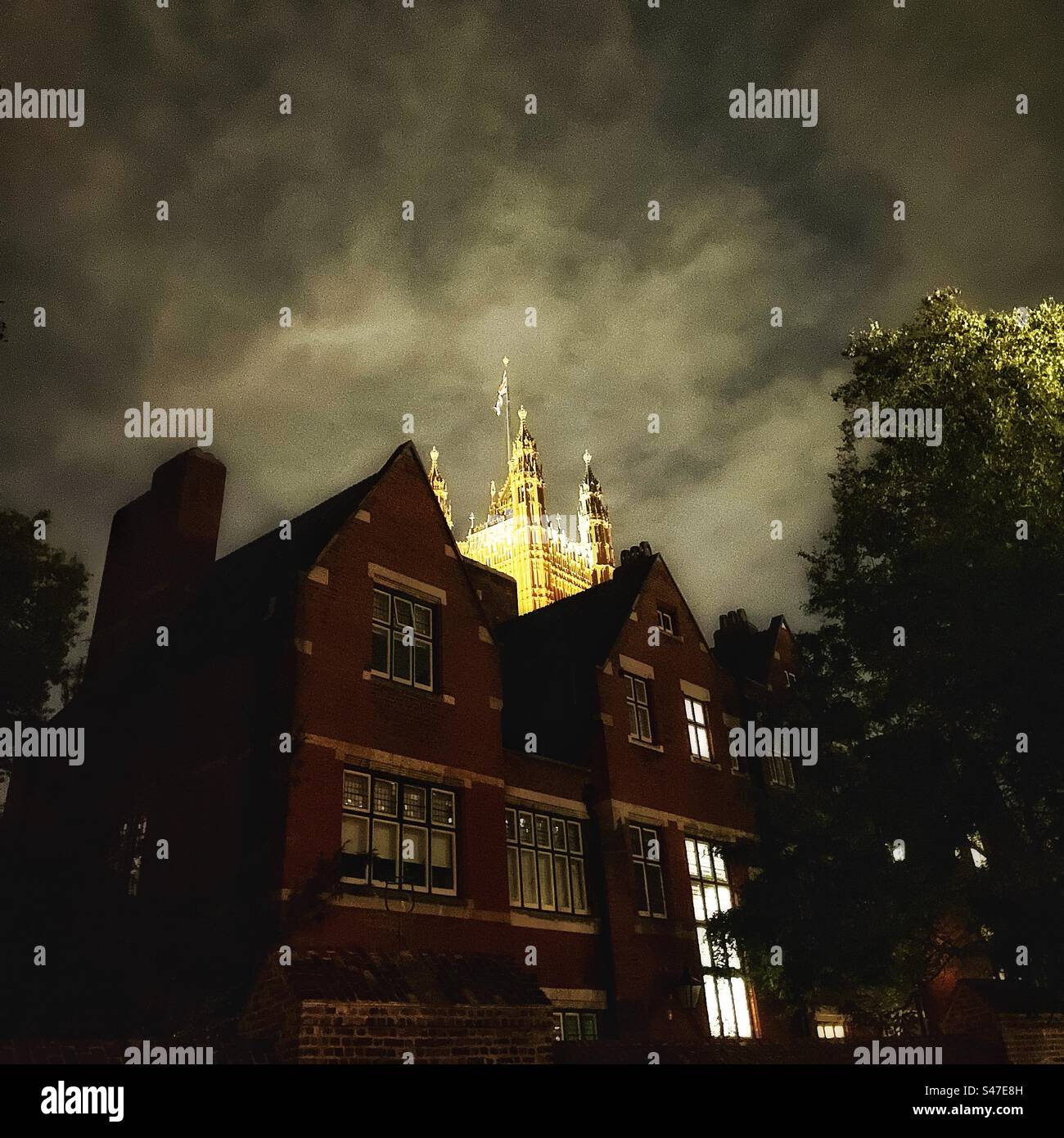 Der Victoria Tower of the Houses of Parliament, der nachts vom Gelände der Westminster Abbey aus mit einer Flagge beleuchtet wurde - Smartphone-aufgenommenes Stockfoto