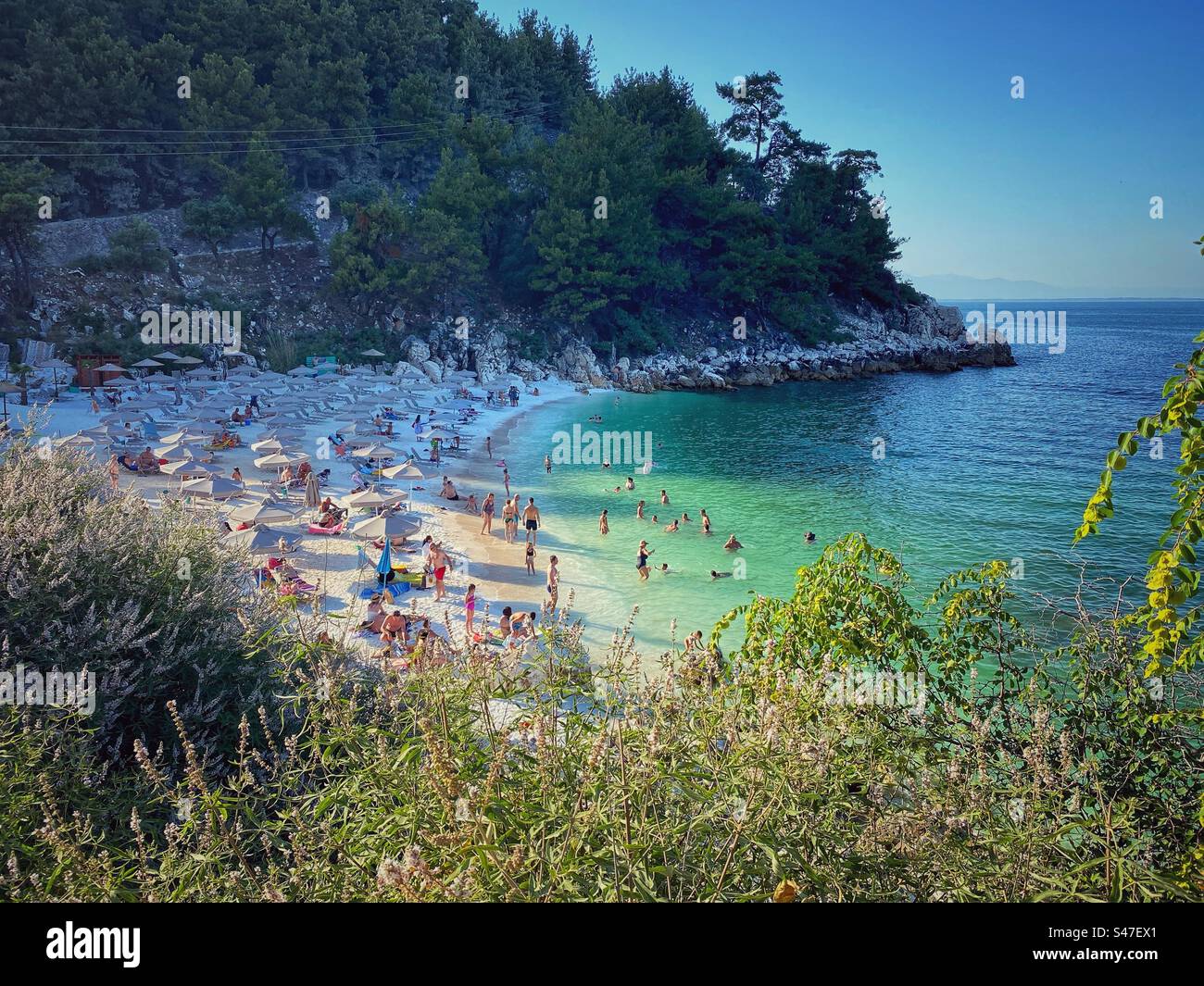 Marmorstrand voller Menschen mit Marmorsand, Steinen und türkisfarbenem Wasser auf der Insel Thassos, Griechenland. - Smartphone-aufgenommenes Stockfoto