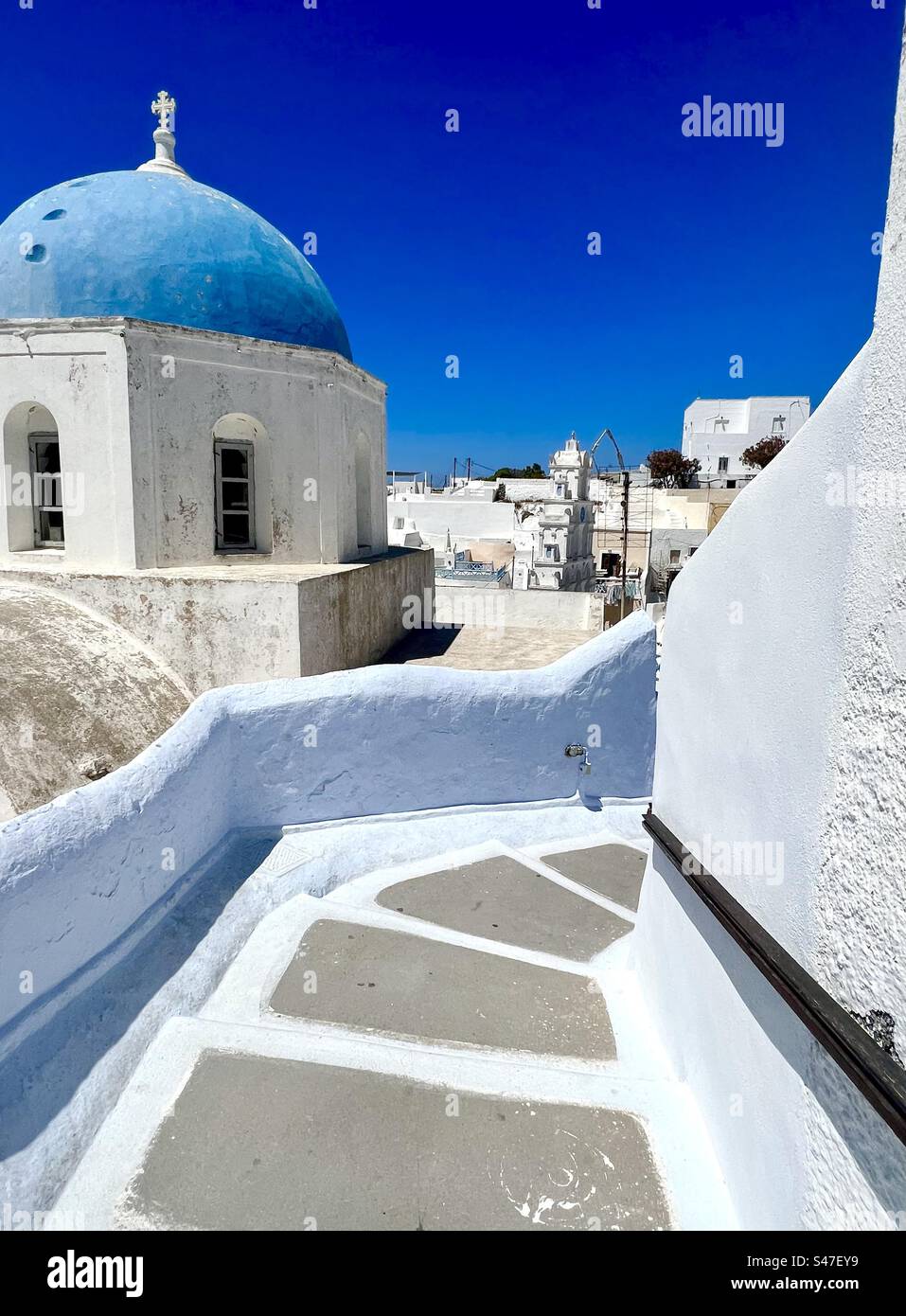 Wände in blassblau und weiß säumen einen gewundenen Treppenpfad, der hinunter zum Zentrum des Dorfes Megalochori führt, vorbei an der blauen Kuppelkirche Zoodochos Pigi. Santorin Stockfoto