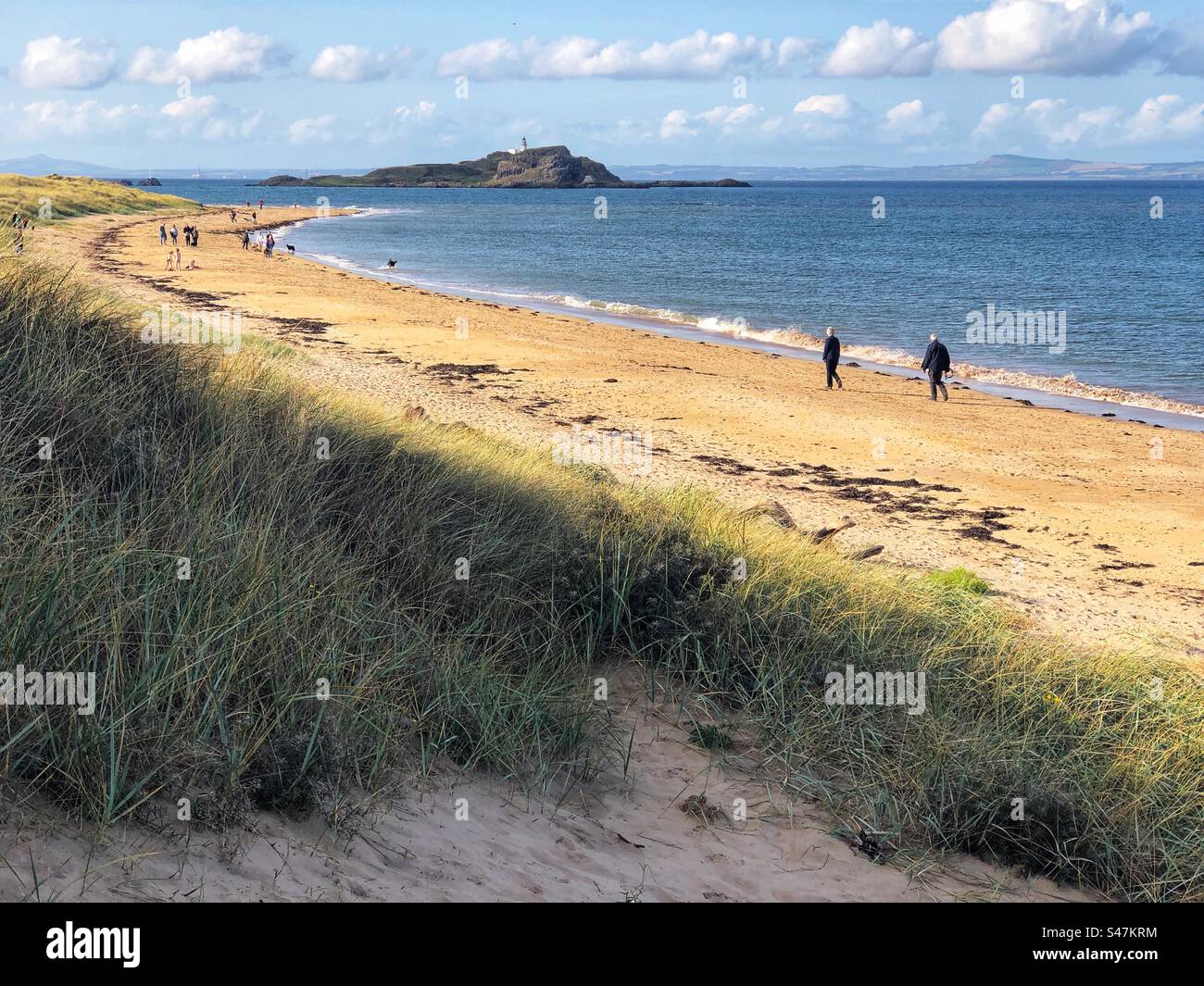 Leute, die am Yellowcraig Beach laufen, mit Blick auf den Leuchtturm Fidra, East Lothian Scotland - Smartphone-aufgenommenes Stockfoto