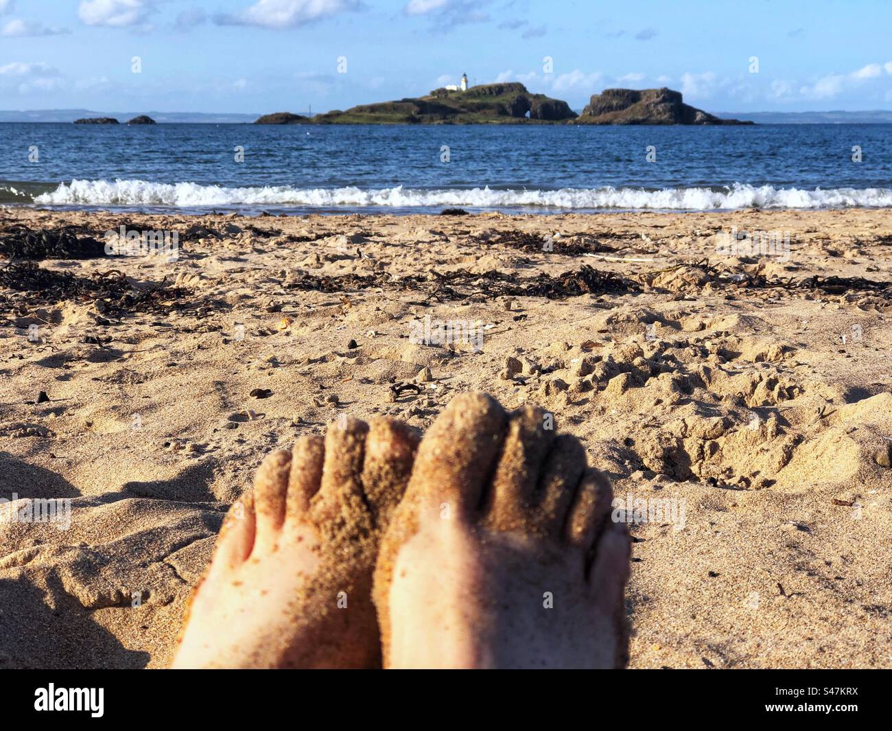 Sitzen Sie am Yellowcraig Beach mit Blick auf den Fidra Leuchtturm in der vierten Mündung, East Lothian Schottland - Smartphone-aufgenommenes Stockfoto