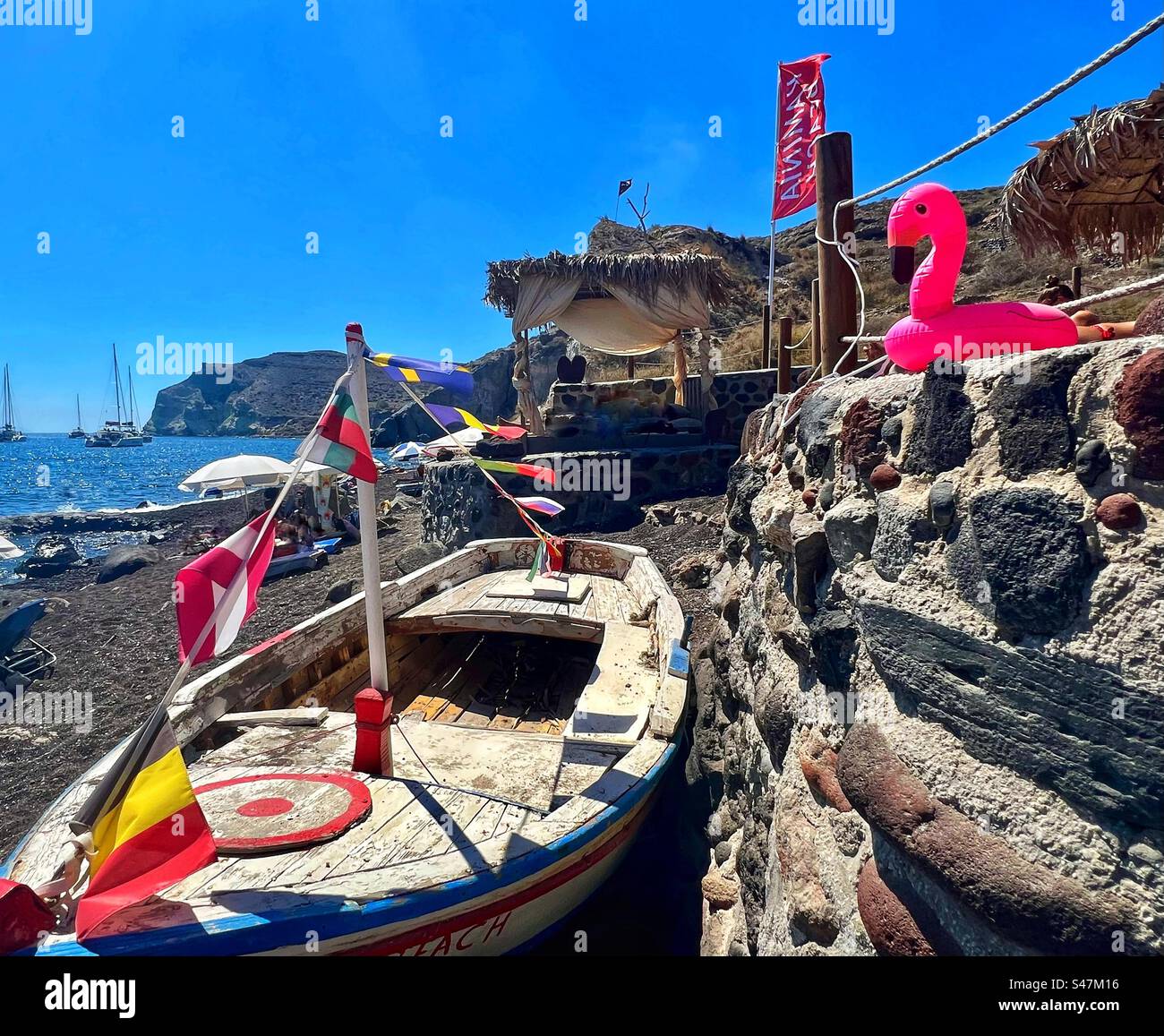 Buntes altes Holzboot und rosafarbenes Flamingowasser schweben auf den Felsen des Kaminia Strandes, in der Nähe des roten Strandes auf Santorin Insel. Stockfoto