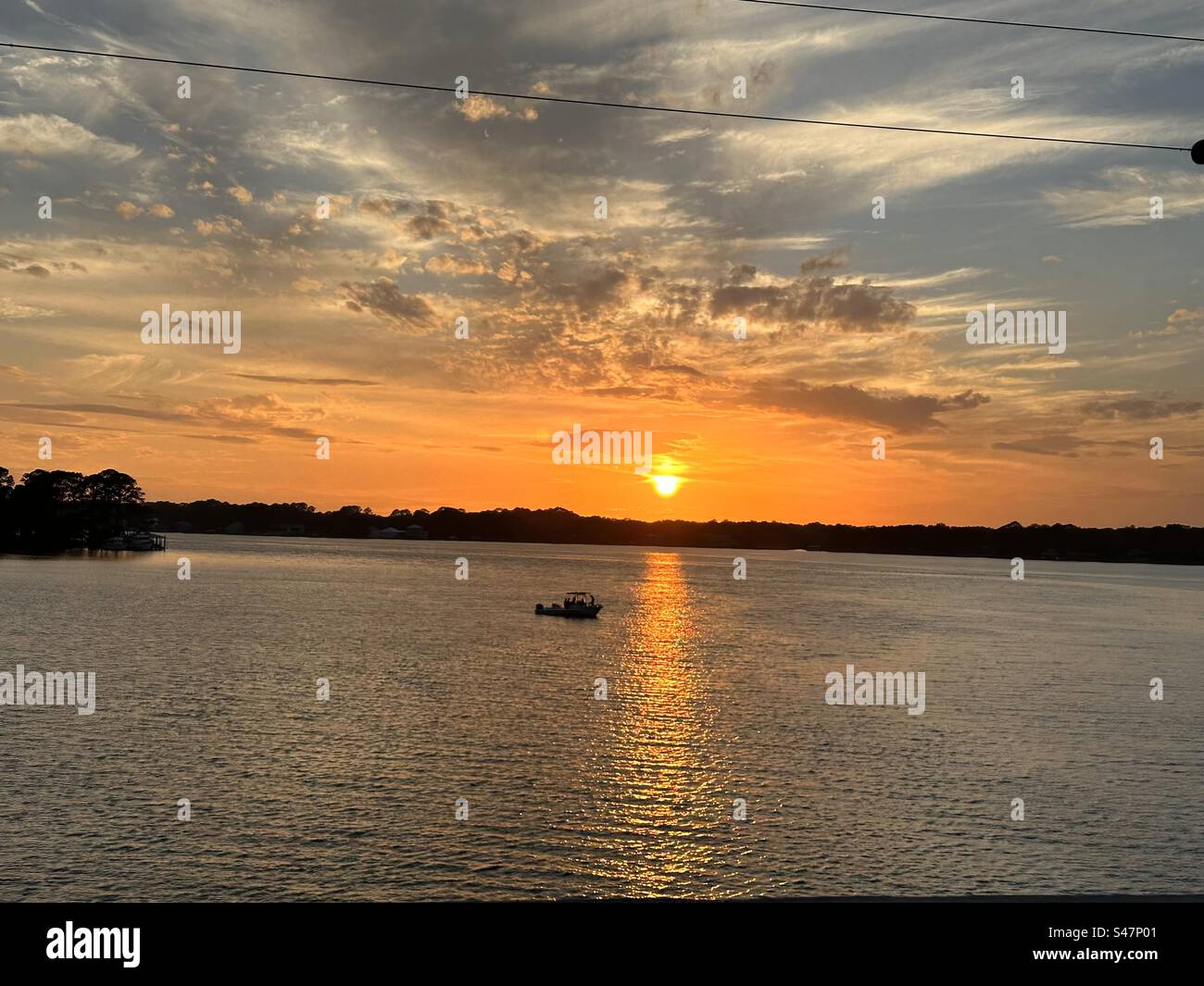 Ein herrlicher und warmer Sonnenuntergang in der Florida Panhandle. Mit einem Fischer, der sich der Sonnenreflexion auf dem Wasser nähert. Stockfoto