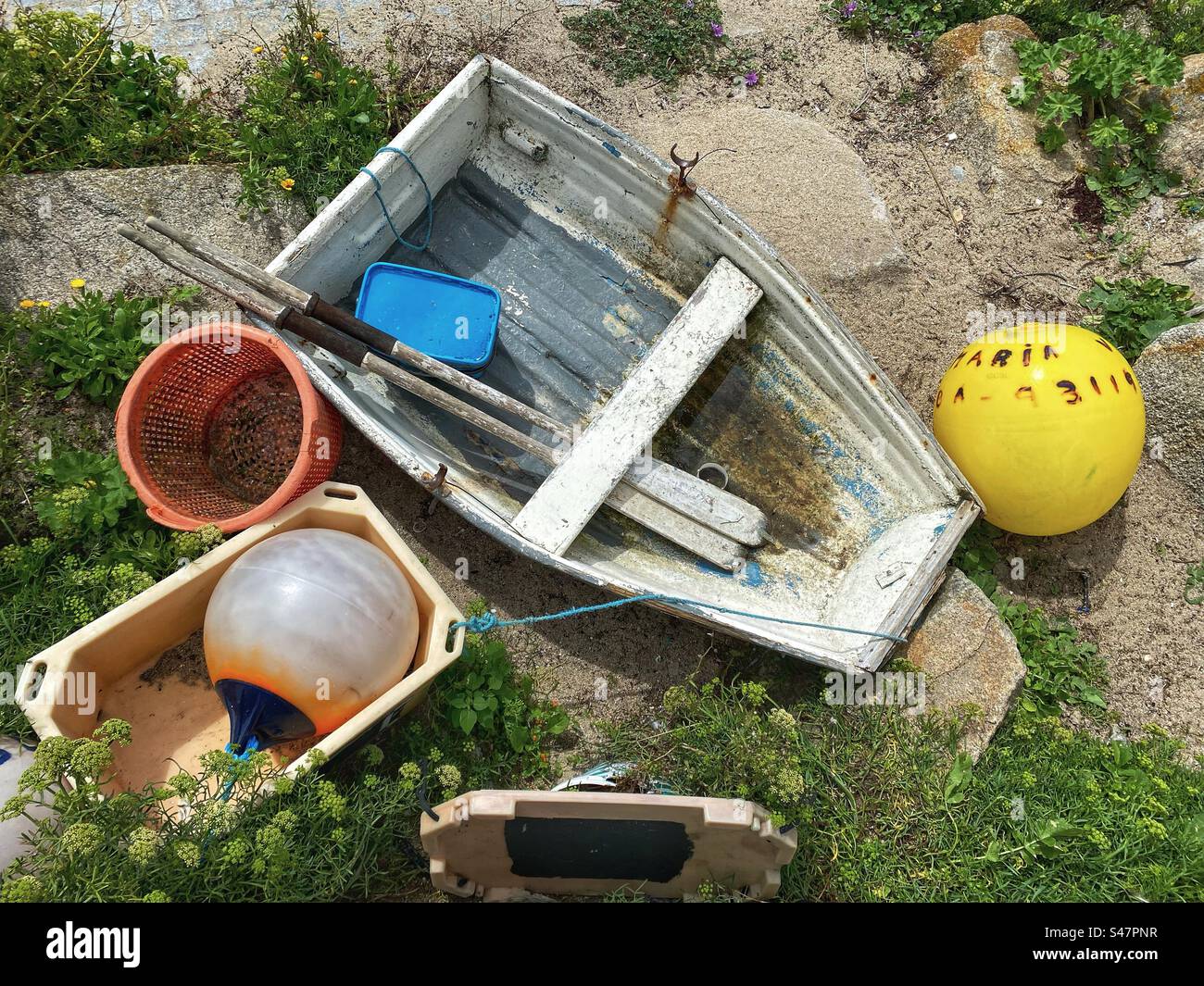 Altes Ruderboot und farbenfrohe Bojen, die am Ufer angespült wurden - Scilly-Inseln, Großbritannien Stockfoto