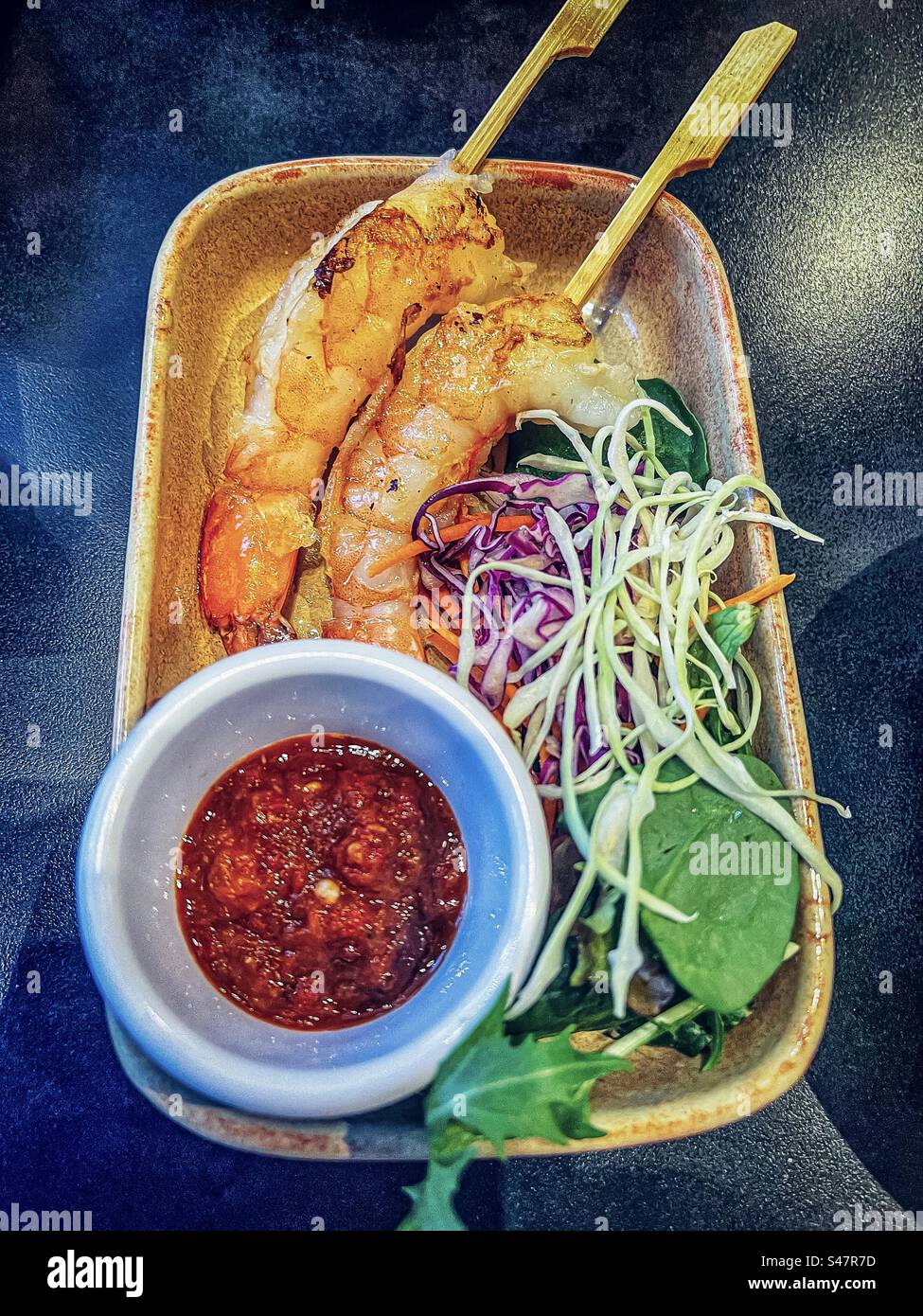 Nahaufnahme mit gegrillten Garnelenspießen und frischem Salat auf Teller mit einer Schüssel scharfer Chili-Sauce auf dem Tisch. Asiatisches Essen. Gesunde Ernährung. Würze. - Smartphone-aufgenommenes Stockfoto