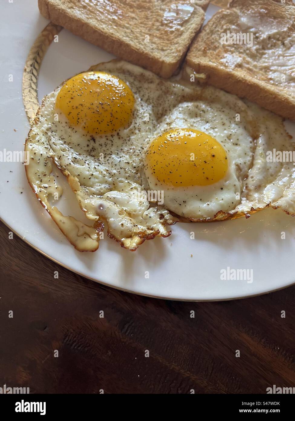 2 sonnige Eier auf weißem Teller mit gebuttertem Toast. Enthält Druckbereich. Stockfoto