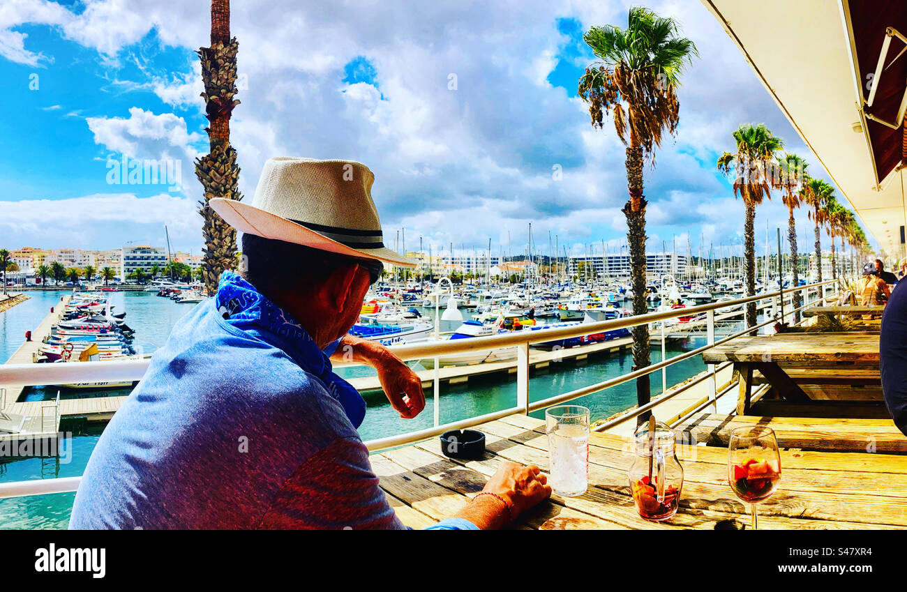 Mann mit Fedora-Hut, der über die Marina in Lagos Portugal schaut - Smartphone-aufgenommenes Stockfoto