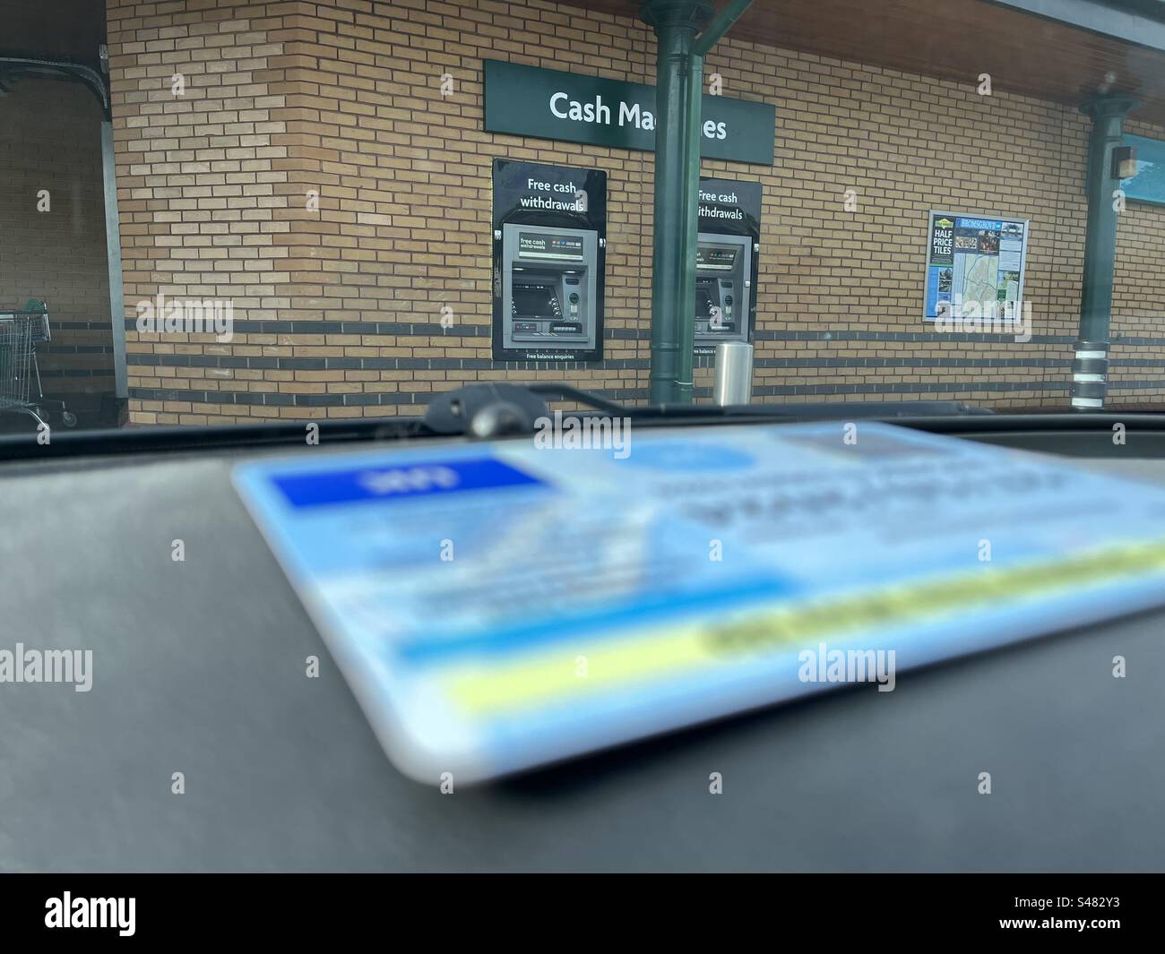 Geldautomaten im Fokus mit blauem Schild für behinderte Fahrer auf dem Armaturenbrett im Auto verschwimmen im Vordergrund. Stockfoto