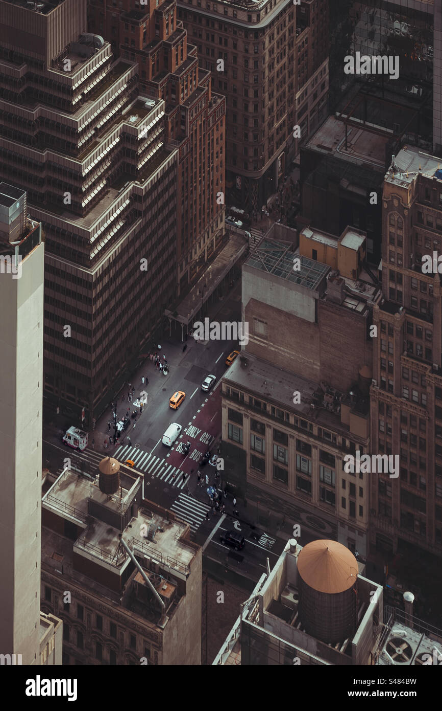 Hoch über New York City mit Blick hinunter zwischen hohen Gebäuden und Wolkenkratzern zu einer Straßenecke mit gelbem Taxi und Verkehr Stockfoto