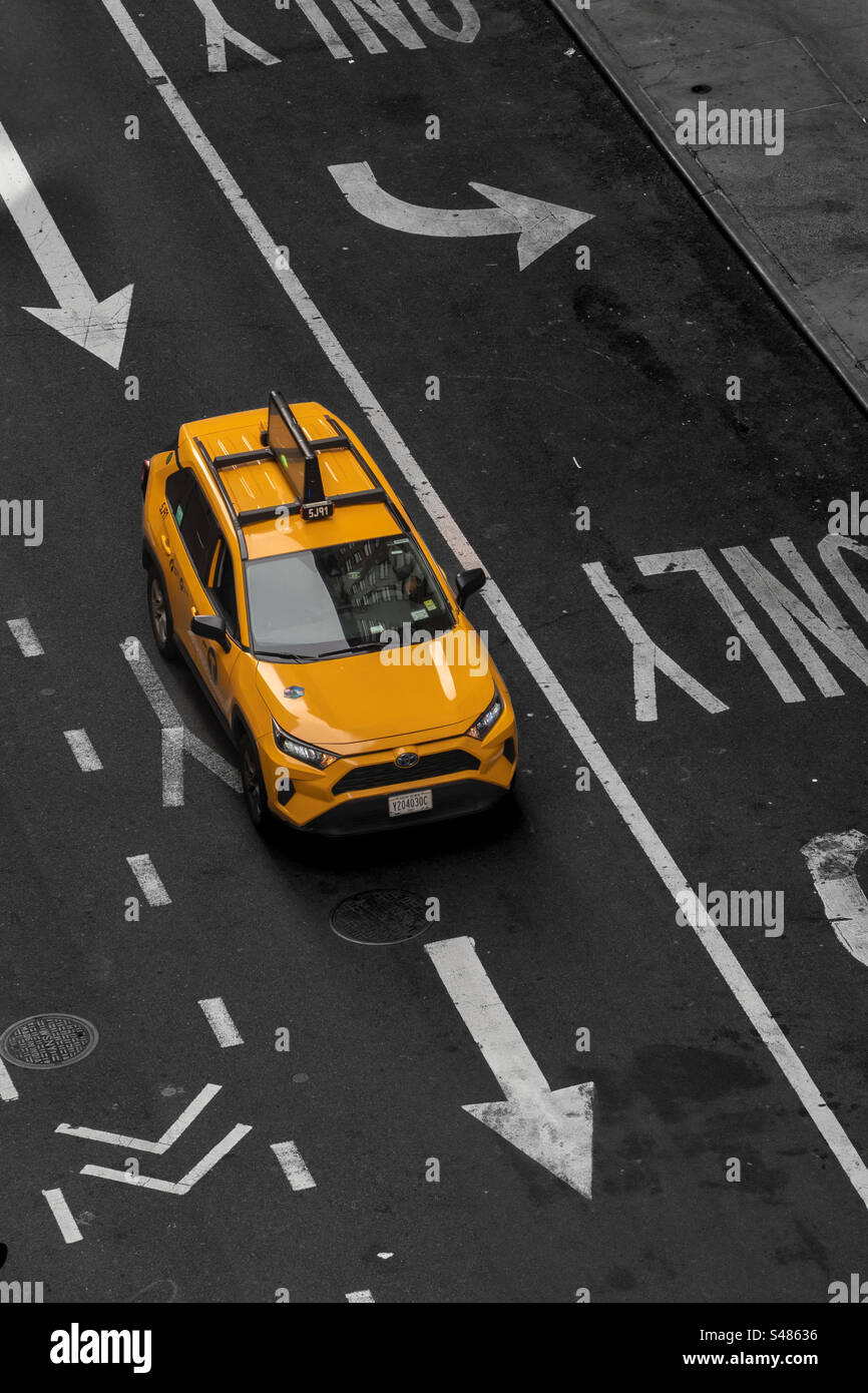 Aus der Vogelperspektive über einem gelben New Yorker Taxi auf einer leeren Straße mit Richtpfeilen und Straßenmarkierungen in New York City mit Kopierraum - Smartphone-aufgenommenes Stockfoto