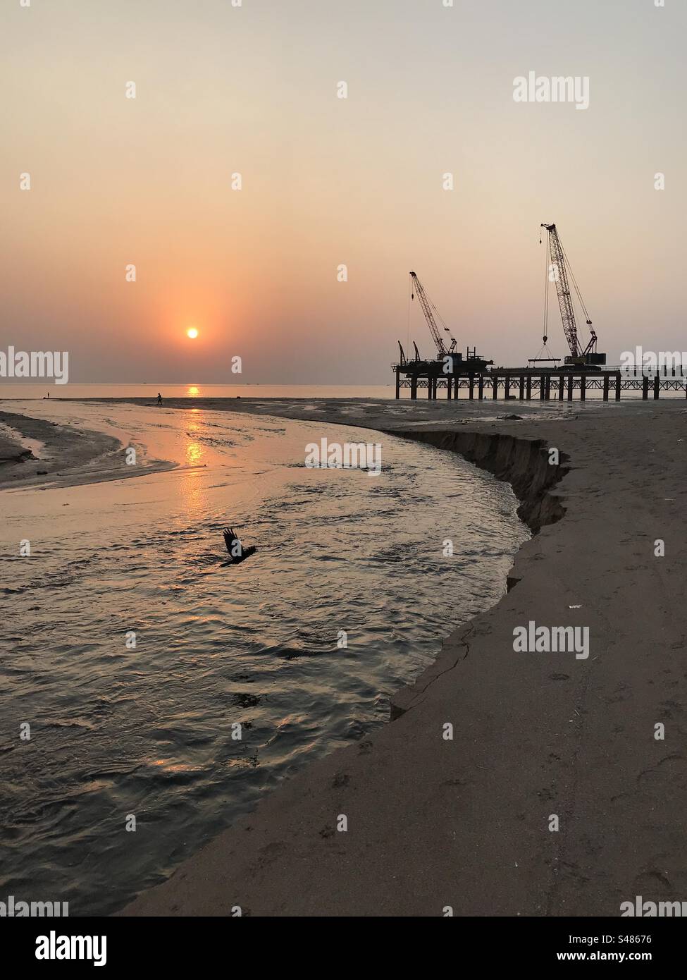 Schwere Maschinen für Straßenbauarbeiten am Strand bei Sonnenuntergang - Smartphone-aufgenommenes Stockfoto