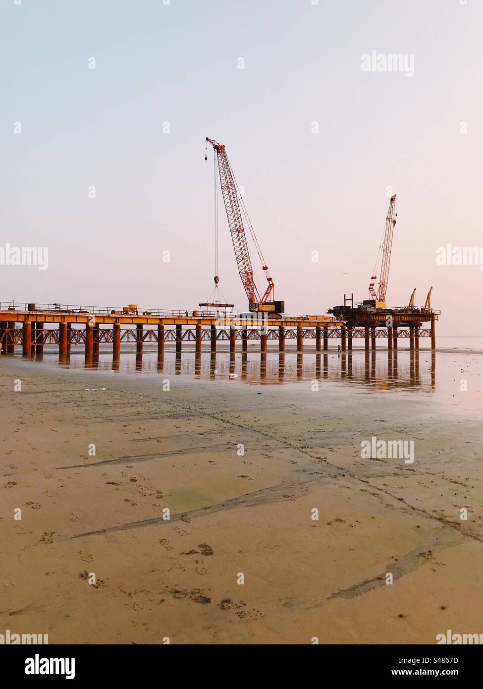Kräne und schwere Bauarbeiten an einem Strand, an dem eine Autobahn gebaut wird - Smartphone-aufgenommenes Stockfoto