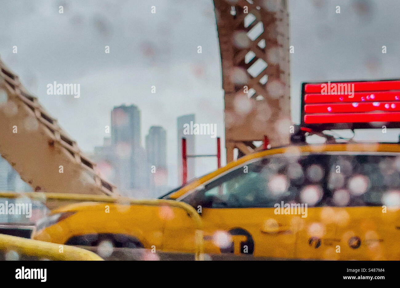 Gelbes New Yorker Taxi überquert die Queensboro Bridge im Regen mit Türmen von Manhattan in der Ferne Stockfoto