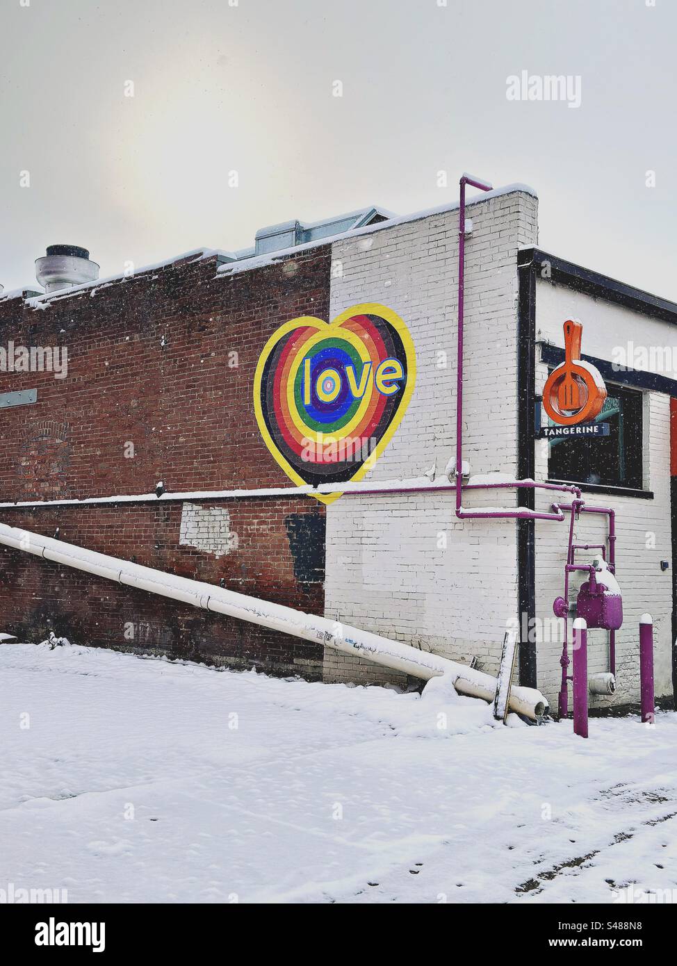 Herzförmiges Liebessymbol an der Wand während des Schneesturms in Longmont, Colorado, USA. Farbenfroher Kontrast zu weiß. Stockfoto