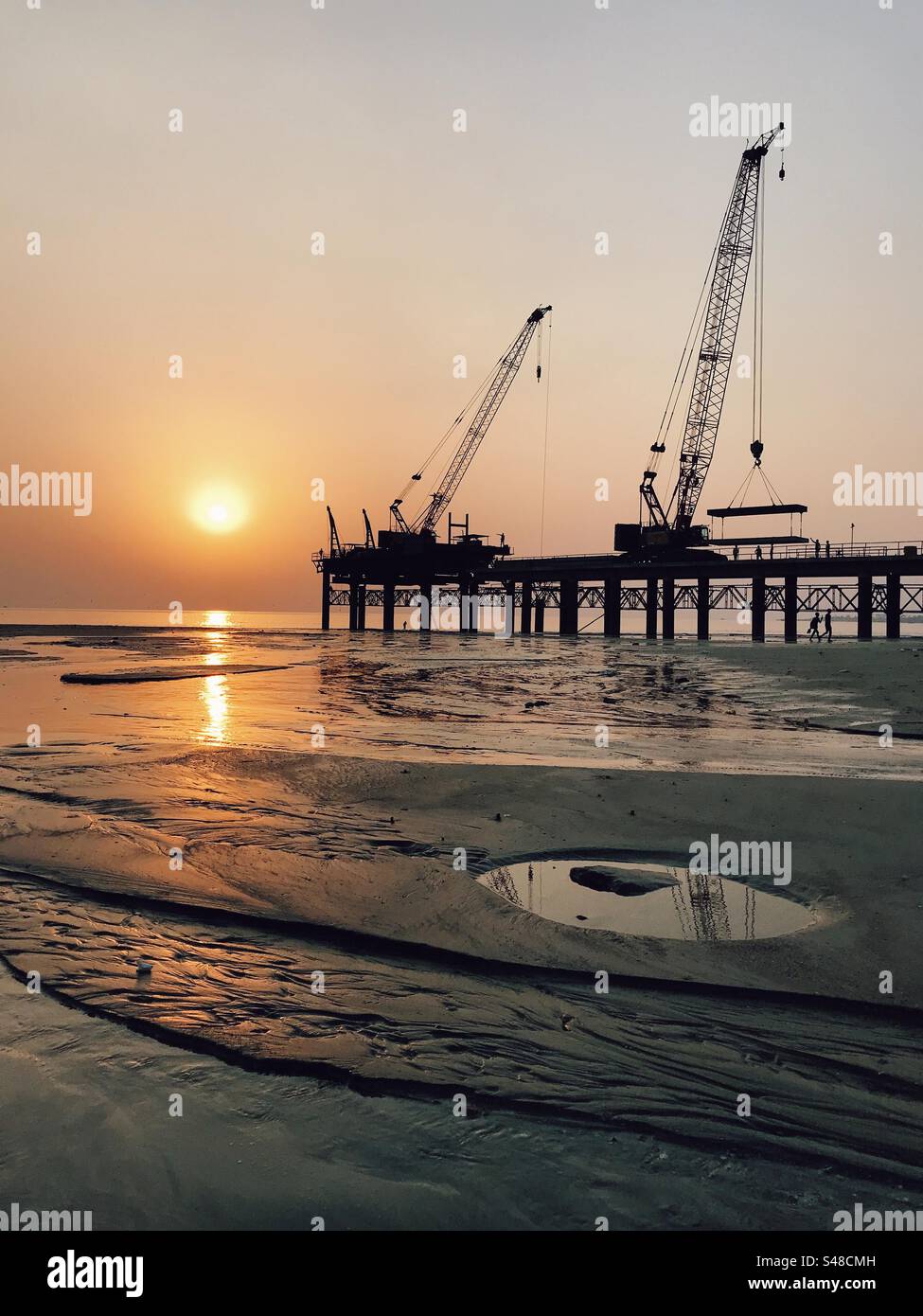 Baukran und Infrastruktur am Strand bei Sonnenuntergang Stockfoto