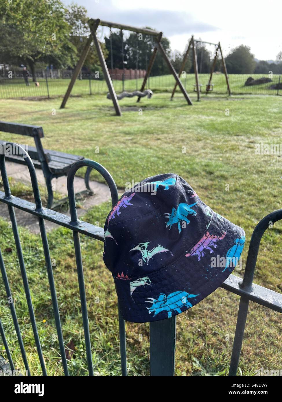 Dinosauriermütze für Kinder auf dem Geländer auf dem Spielplatz - Smartphone-aufgenommenes Stockfoto