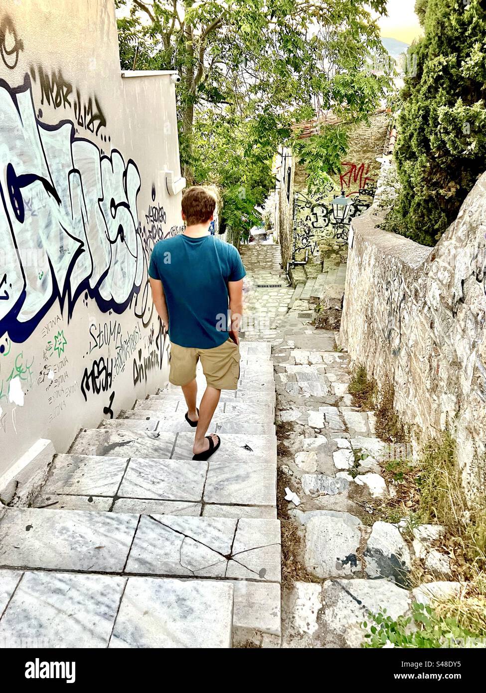 Junge Männer, die eine enge Straße mit steilen Stufen im Plaka Viertel von Athen hinunterlaufen - Smartphone-aufgenommenes Stockfoto