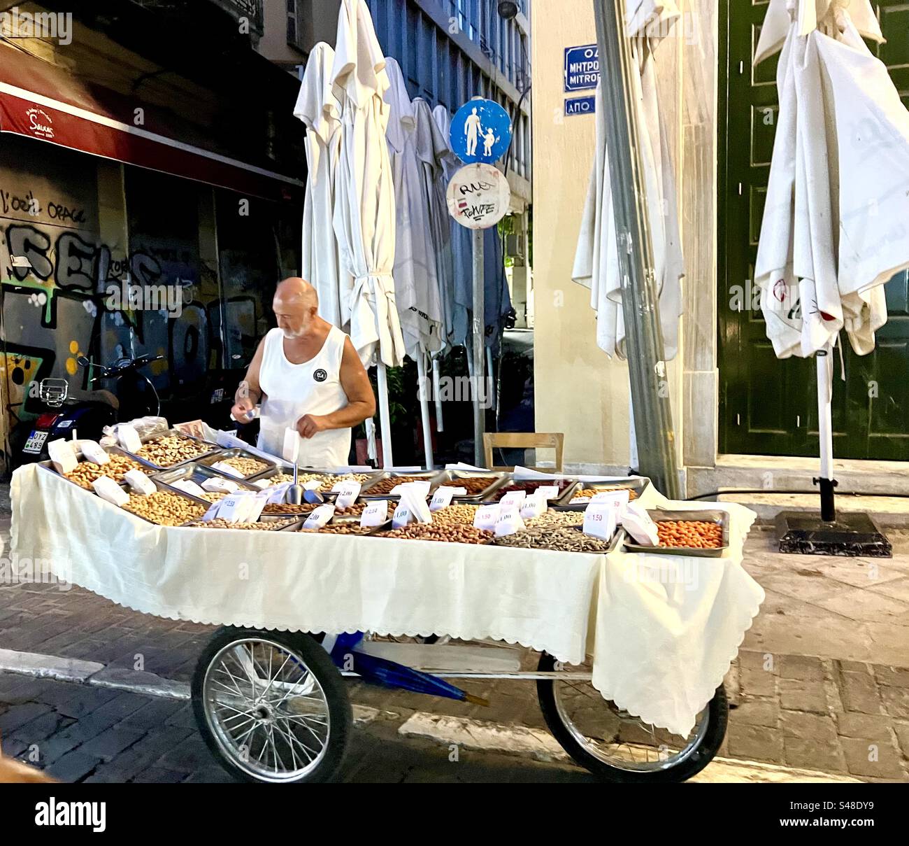 Straßenverkäufer draußen auf der Mitropoleos Straße in der Nähe des Monastiraki Platzes, der abends Snacks aus seinem Wagen verkauft - Smartphone-aufgenommenes Stockfoto