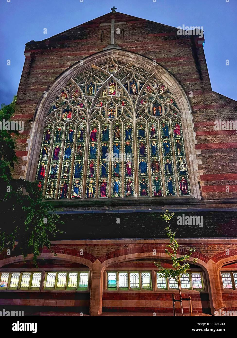 Der Holy Trinity Sloane Square wurde auch als Cathedral of the Arts and Crafts Movement von der Straße aus gesehen nach ihrem Architekten benannt. Feine Buntglasfenster, beleuchtet bei Nacht, Chelsea, London. Stockfoto