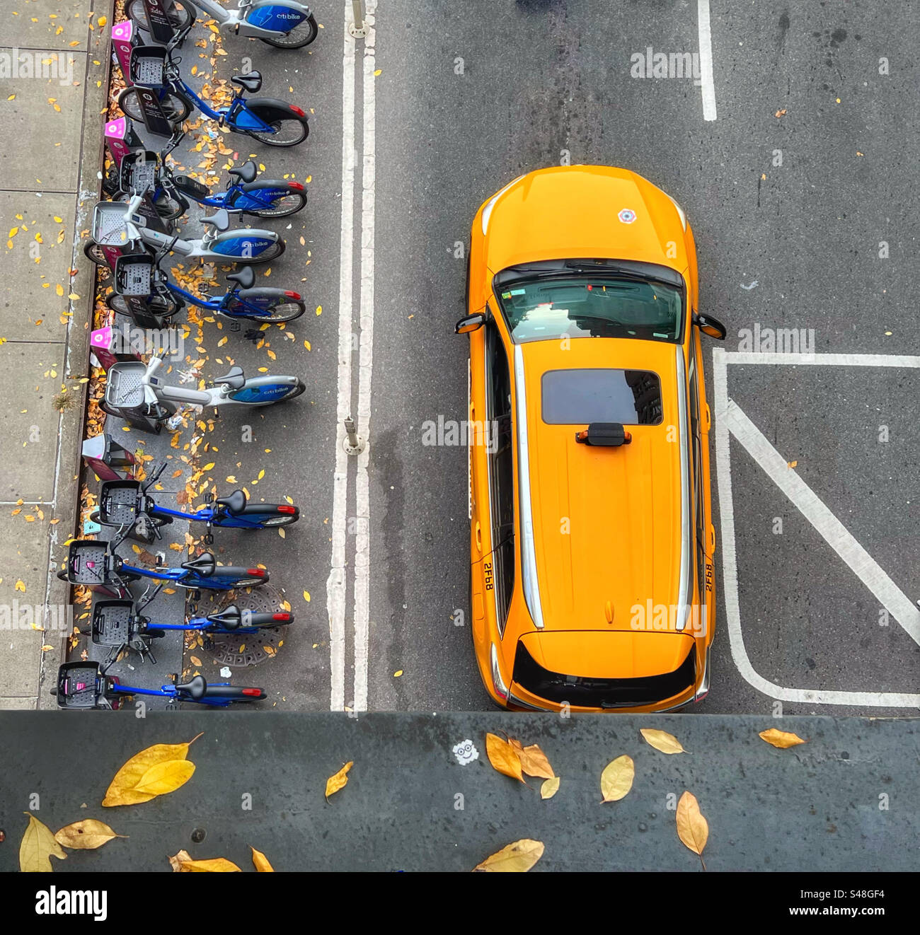 Gelbes New York Taxi von oben an der Kreuzung neben einer Reihe Citibikes zum Verleih - Smartphone-aufgenommenes Stockfoto