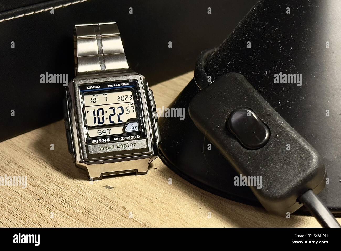 Silberne quadratische Casio WaveCeptor Uhr auf einem schwarzen seitlichen Tischlampen-Schalter. Stockfoto