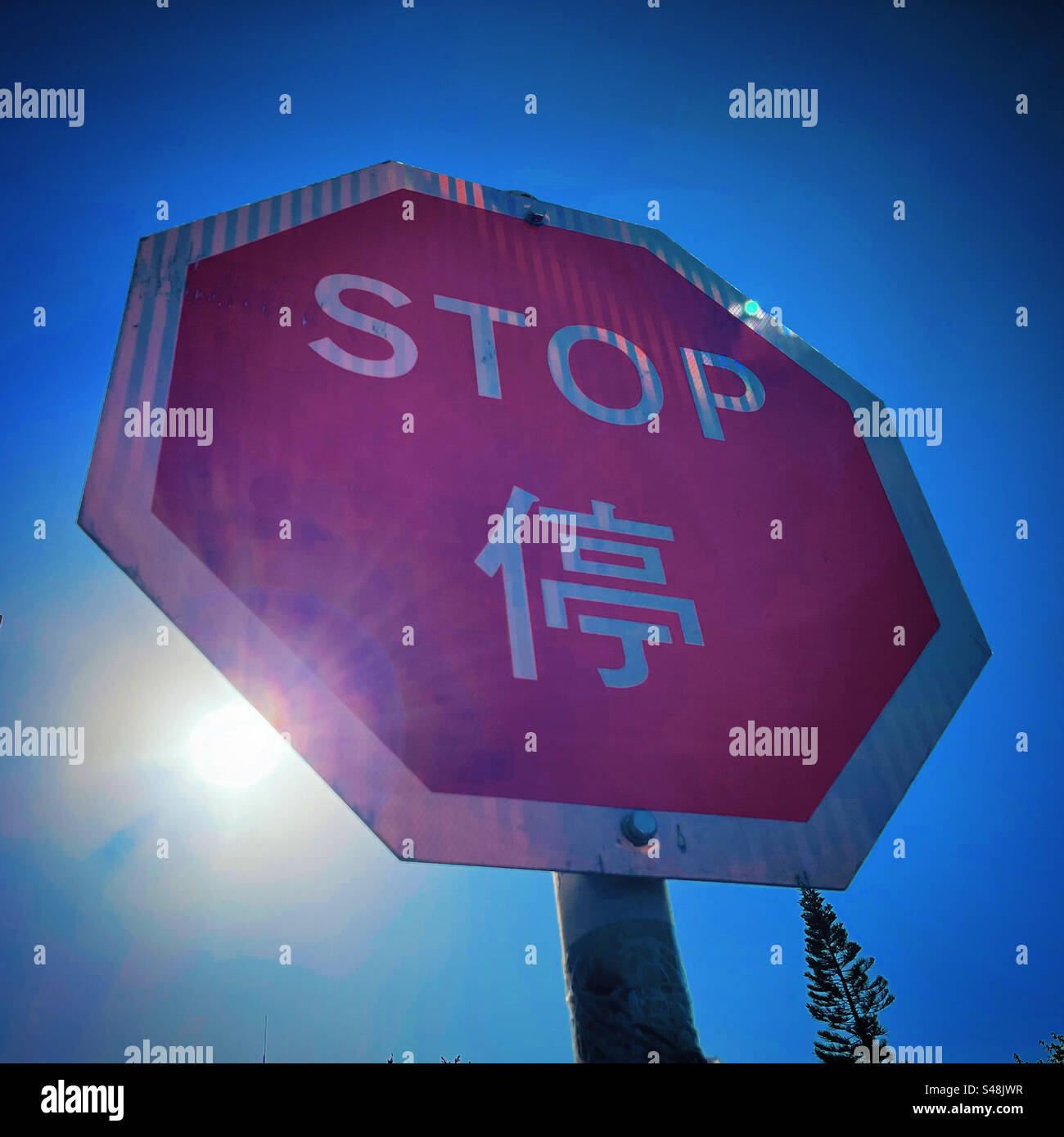 Halten Sie das Straßenschild von hk mit einem Sonnenstrahl in einem dynamischen Winkel vor einem klaren blauen Himmel während des Tages aus nächster Nähe an Stockfoto