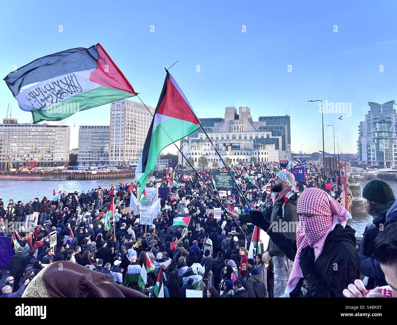 Der Mann in Keffiyeh weht die palästinensische Flagge beim marsch für Palästina in London am 11. November 2023 auf der Vauxhall Bridge vor dem MI6-Hauptquartier Stockfoto
