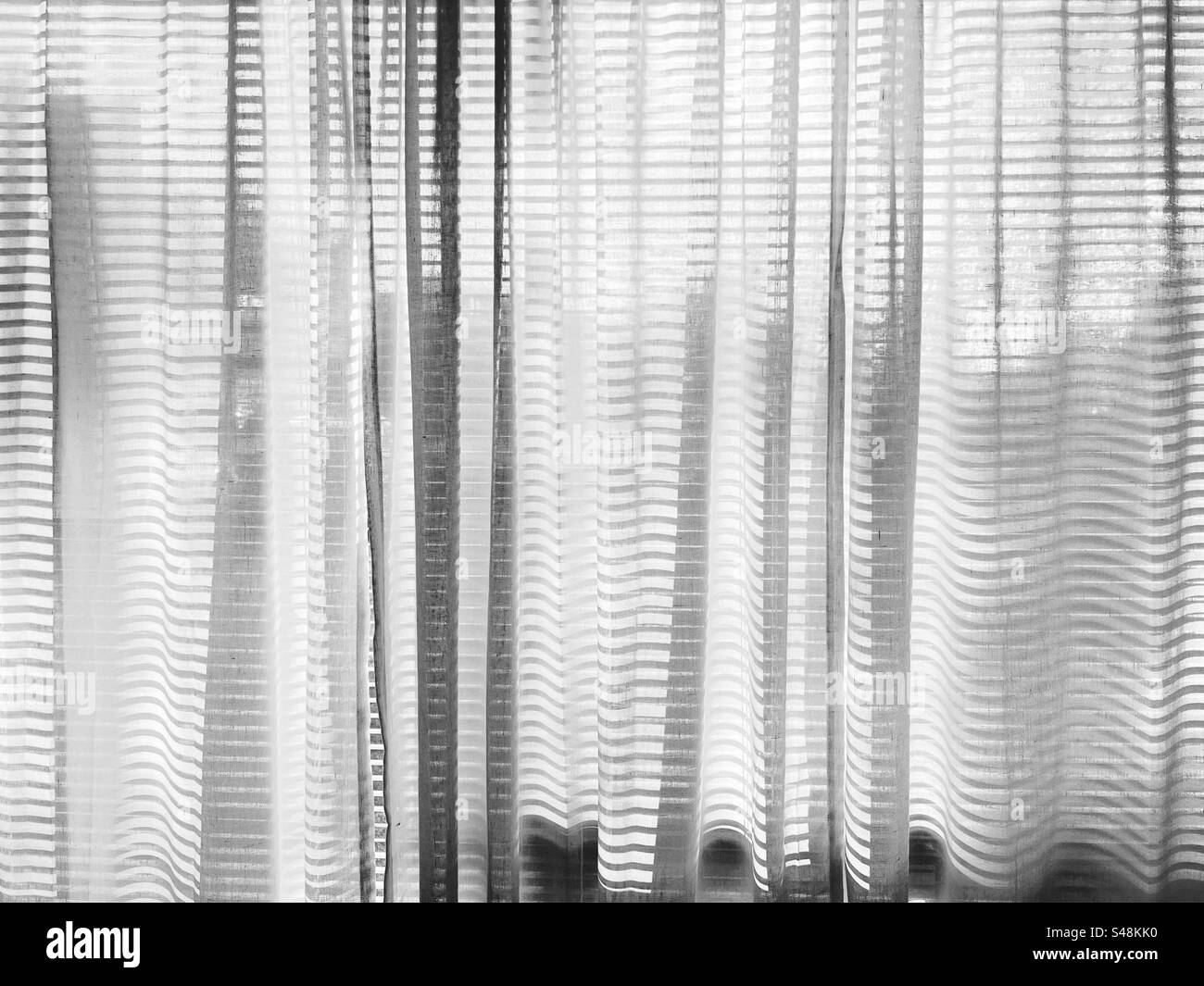 Licht, das durch ein Fenster mit einer venezianischen Jalousie und Baumwollvorhängen leuchtet. Stockfoto