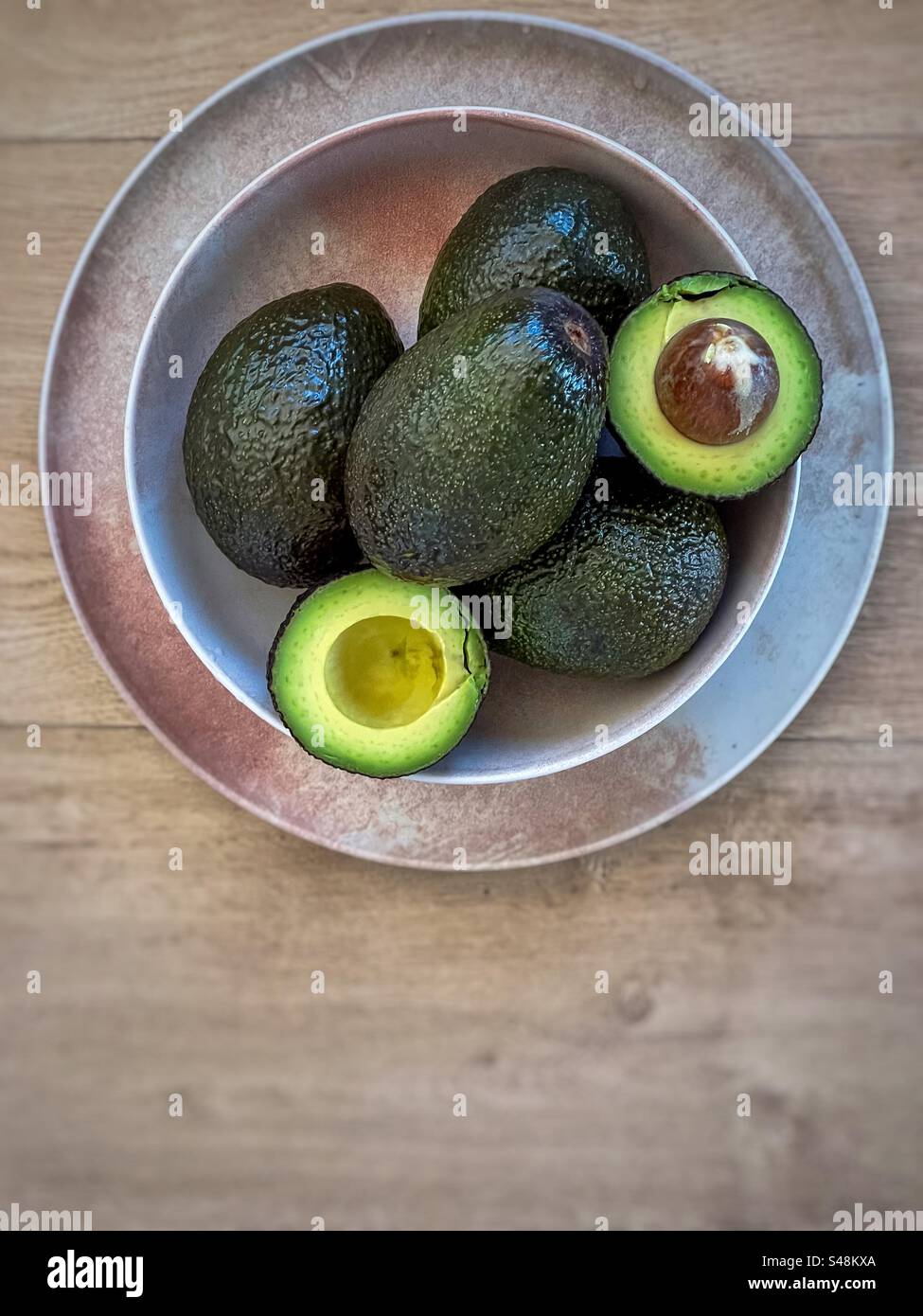 Avocados ganz und in Schüssel auf Teller mit Kopierraum schneiden. - Smartphone-aufgenommenes Stockfoto