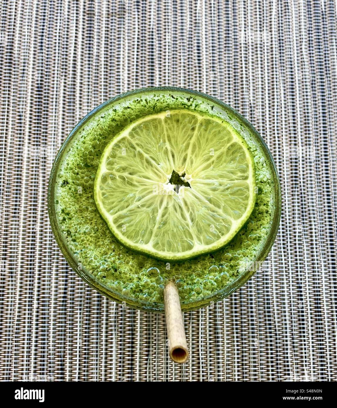 Erfrischendes Getränk aus Passionsfrucht und Minze mit einer Scheibe Limette und einem Papierstroh. - Smartphone-aufgenommenes Stockfoto