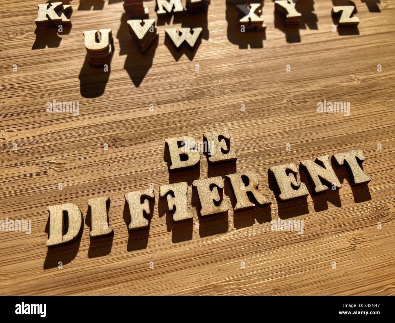 Seien Sie anders, Wörter in hölzernen Buchstaben, die auf dem Hintergrund als Bannerüberschrift isoliert sind Stockfoto