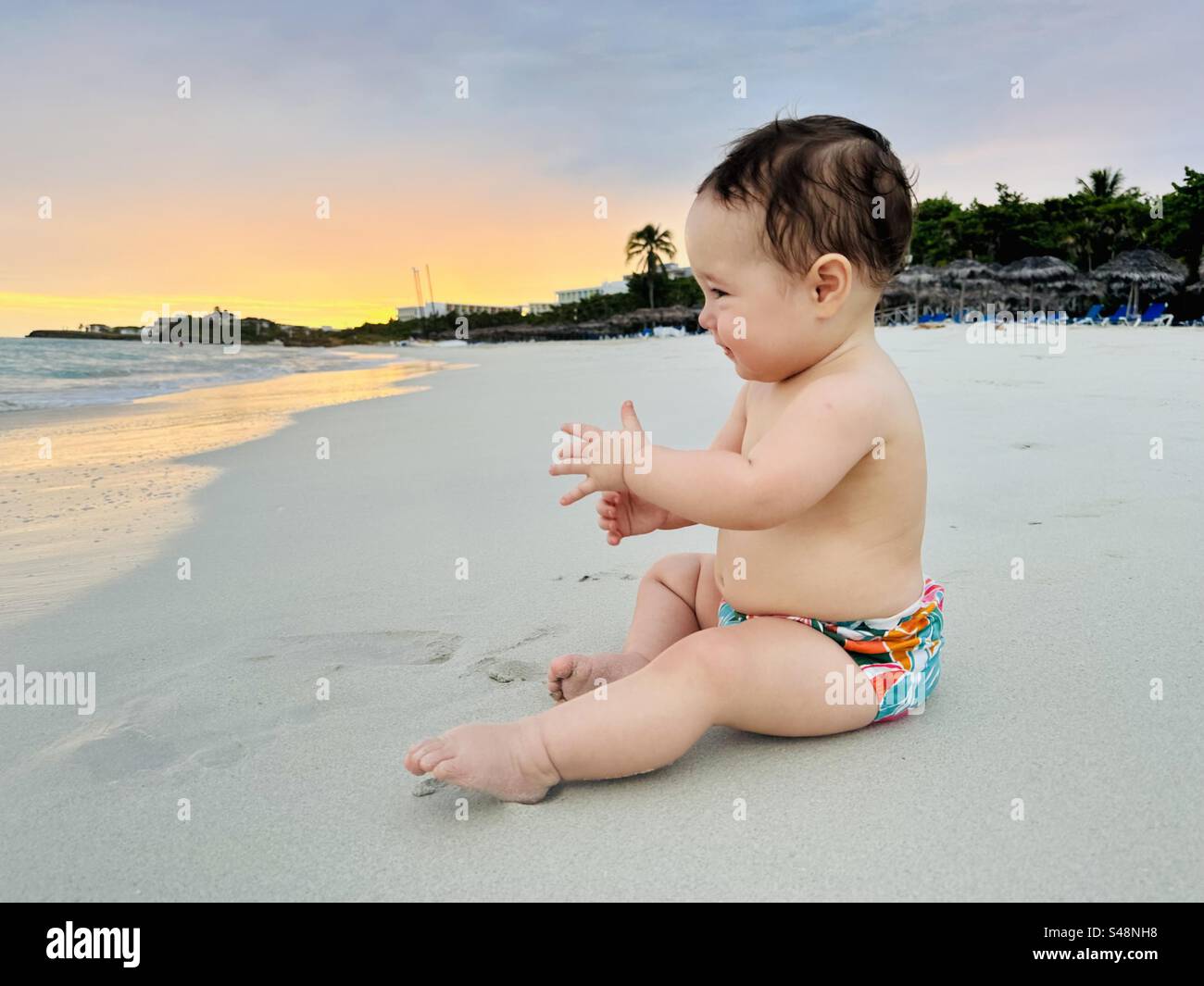 Strandausflug mit Baby. Glückliches Baby, das auf dem Sand sitzt. Varadero, Kuba Stockfoto