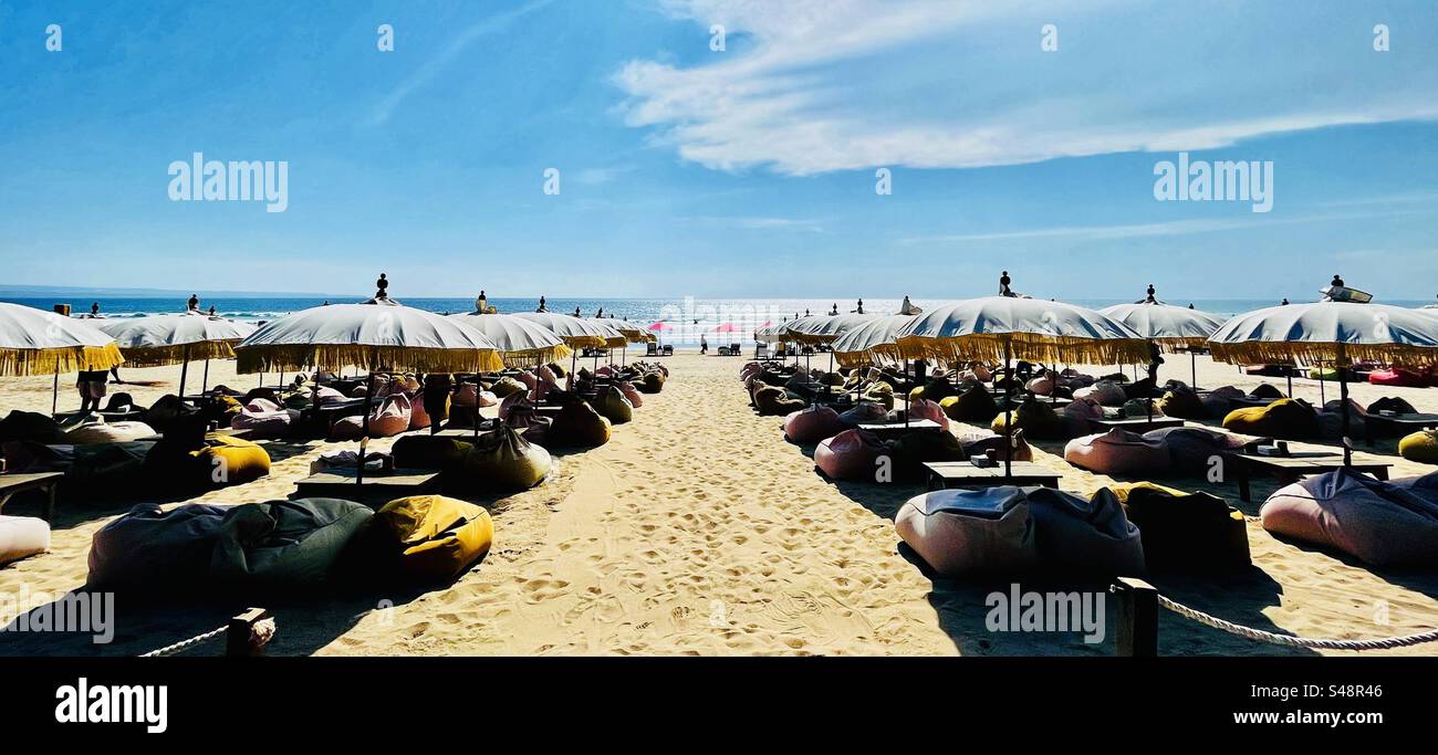 Panoramaaufnahme der Strandbar in Seminyak Bali, bereit für Drinks bei Sonnenuntergang mit Sonnenschirmen und Sitzsäcken Stockfoto